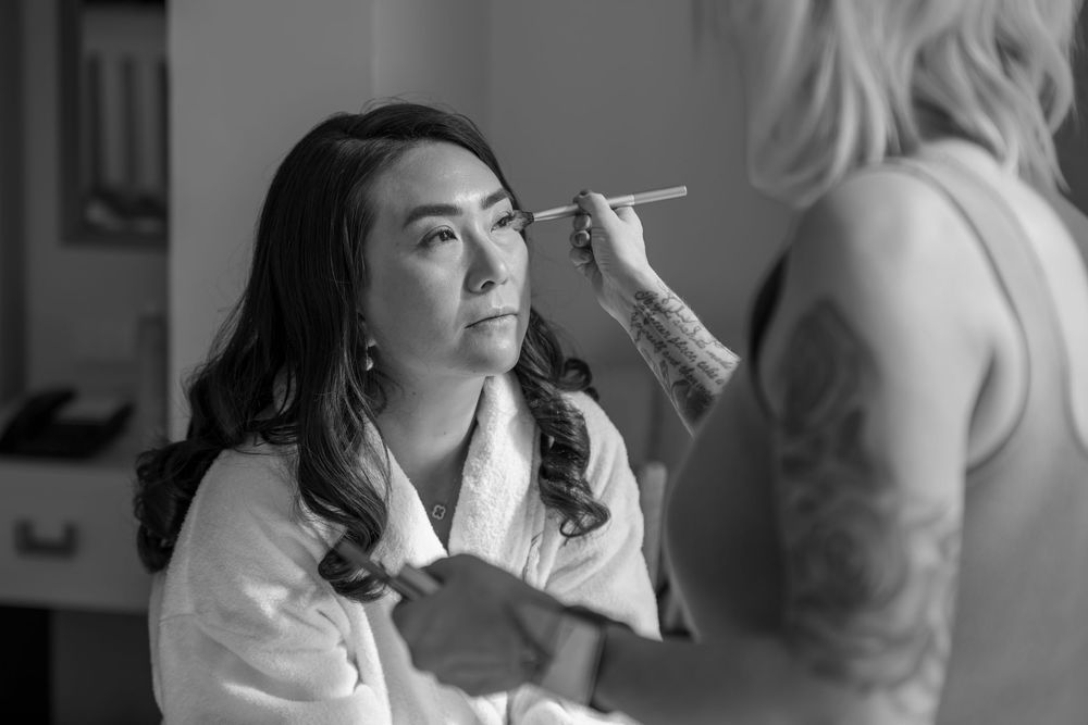 Black and white image of a makeup artist applying cosmetics to a person wearing a white robe.
