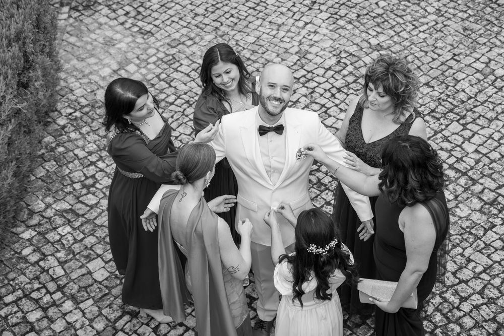 A small wedding party gathered in a circle on a stone paved courtyard, with attendants in dark dresses and one in white.