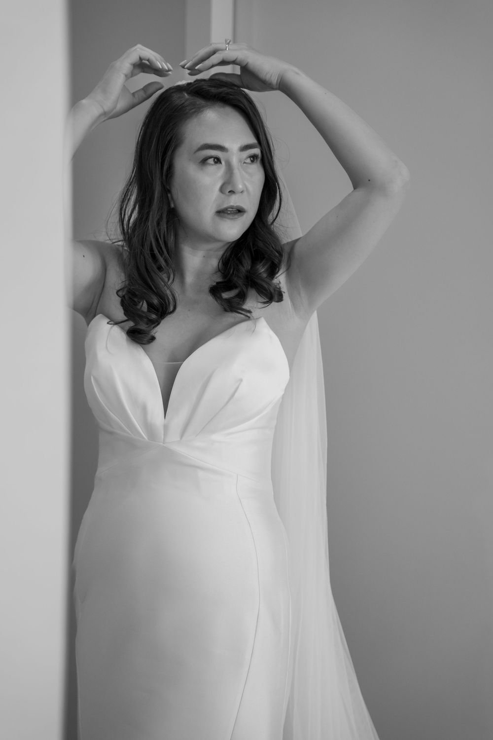 Black and white portrait of a model in an elegant white dress posing gracefully against a wall.