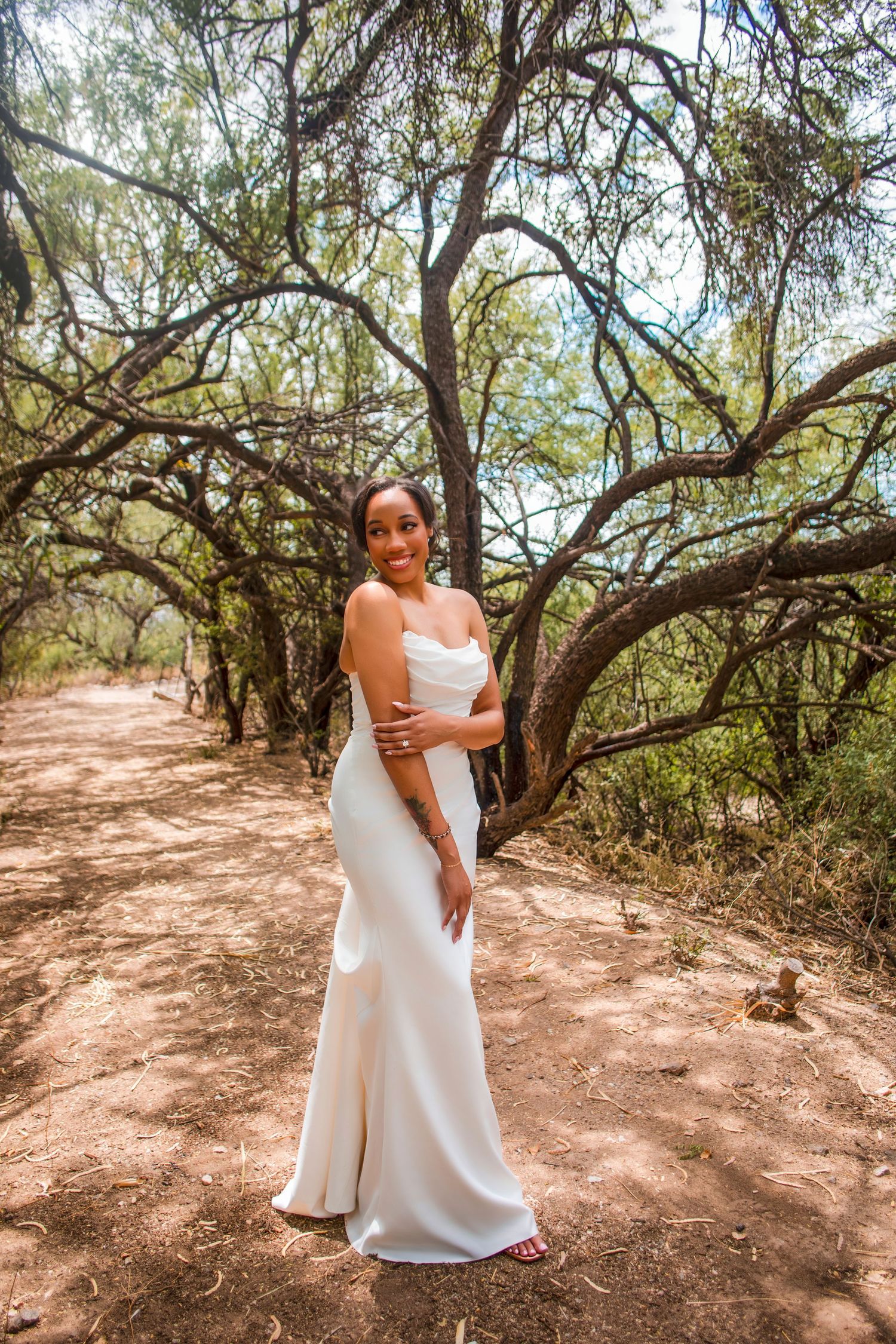 Person in flowing white dress walking along a sunlit dirt path under trees.