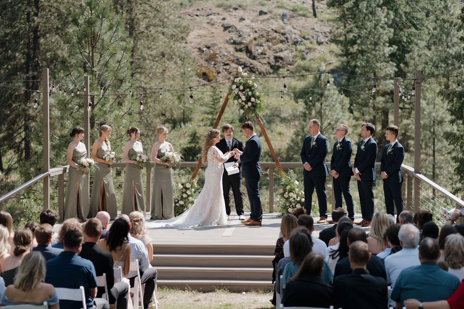 A romantic garden wedding portrait featuring a bride in a lace gown with long train and groom in navy suit under an archway.