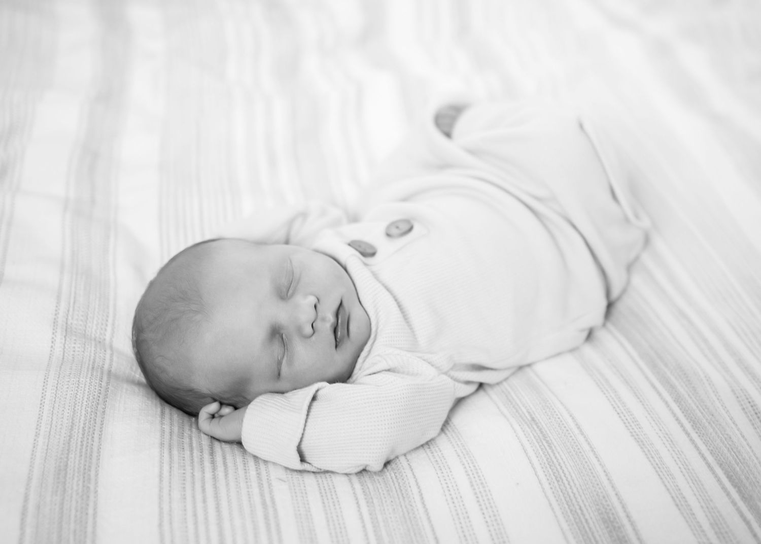 A sleeping newborn baby wrapped in white swaddle blankets rests peacefully on light colored bedding. Lifestyle In-home Newborn Photography.