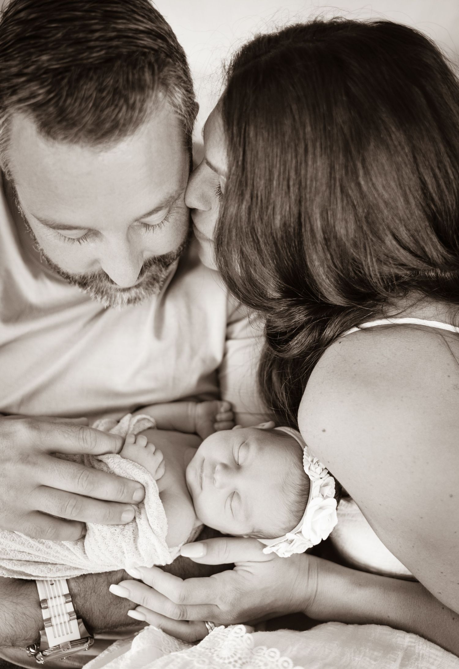 A tender black and white photo series showing a newborn baby being gently kissed in sequence.