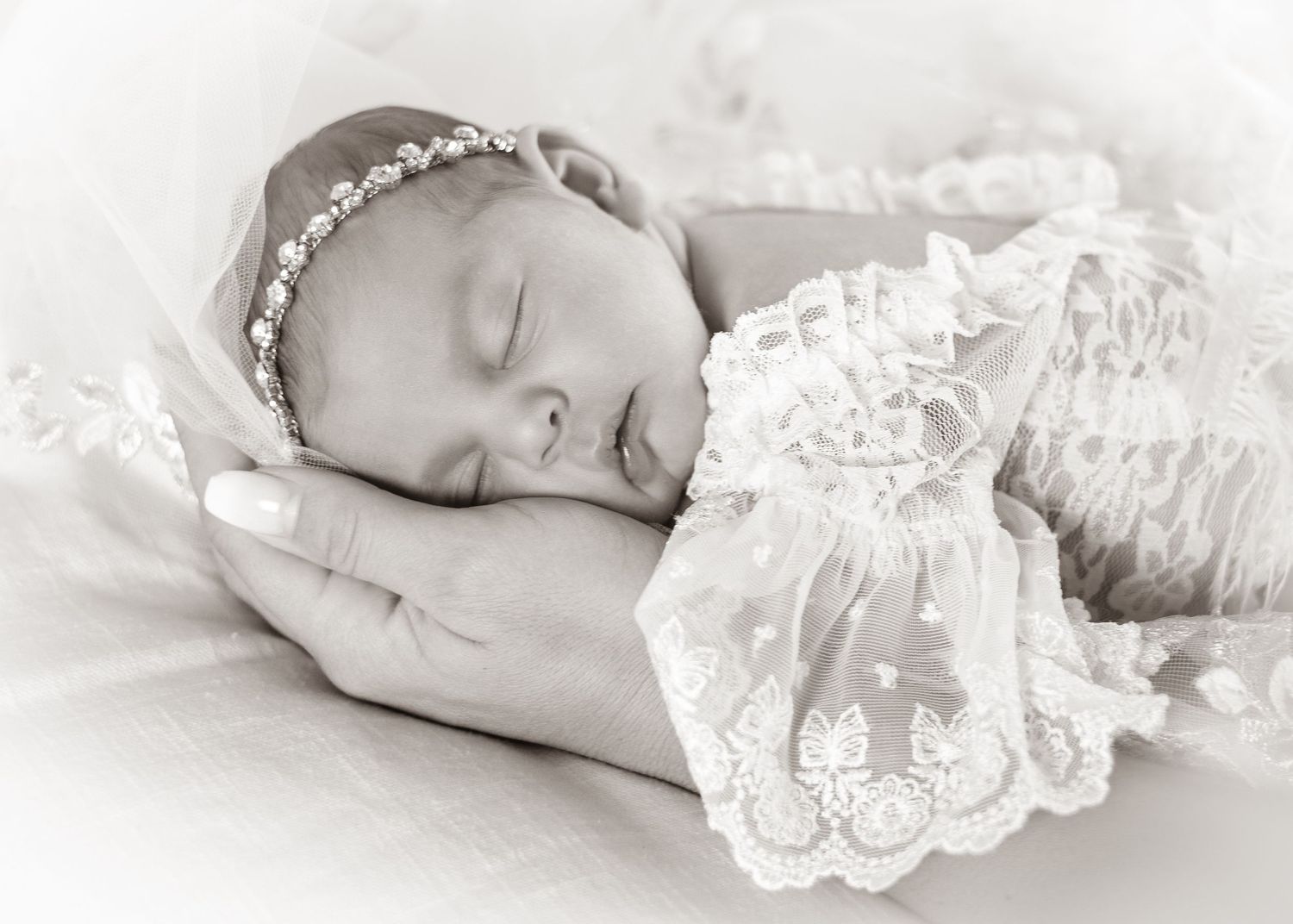 Sleeping newborn baby wrapped in delicate white lace photographed in black and white.