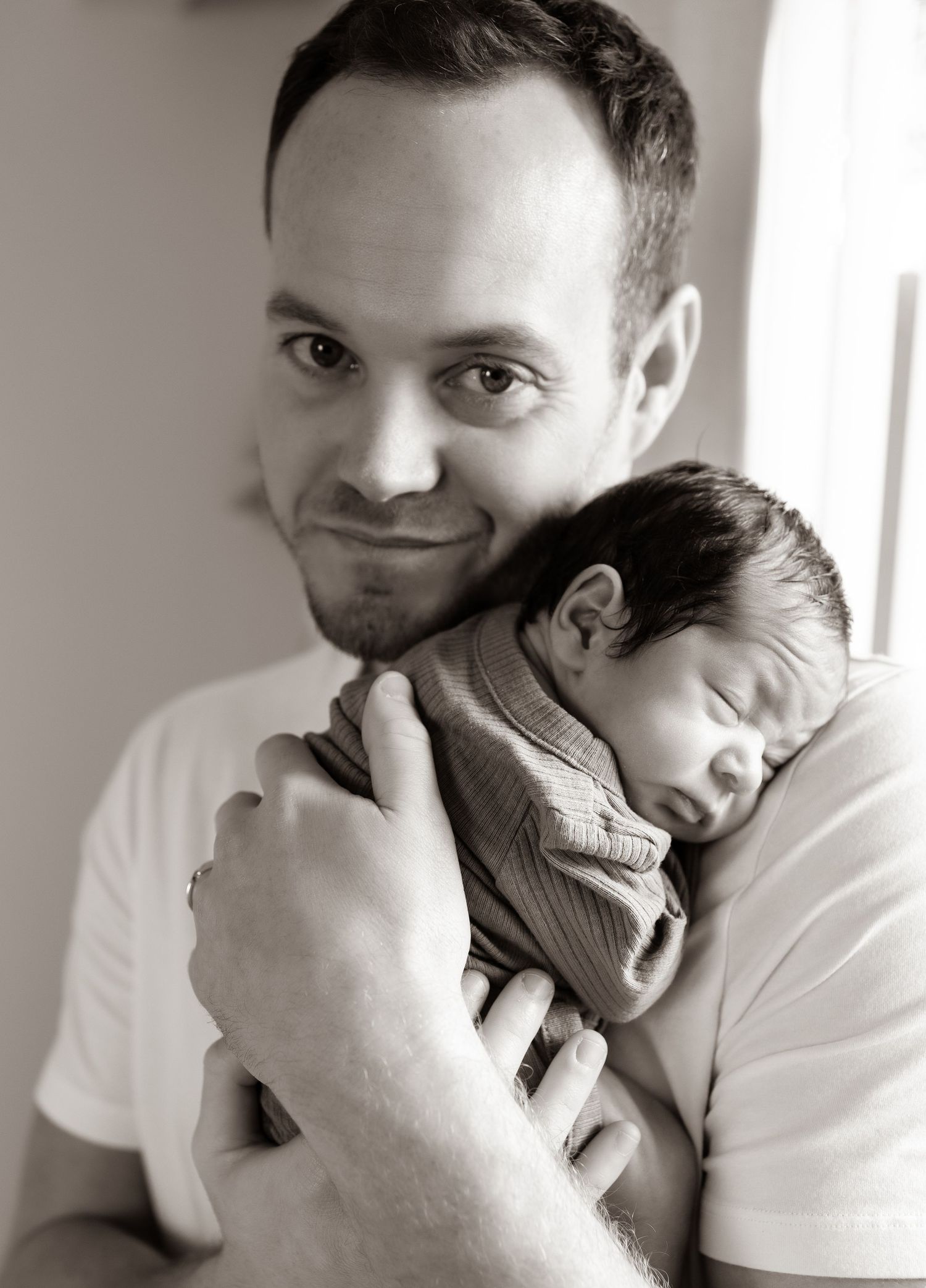 Black and white photo showing tender moments between a dad and sleeping newborn baby.