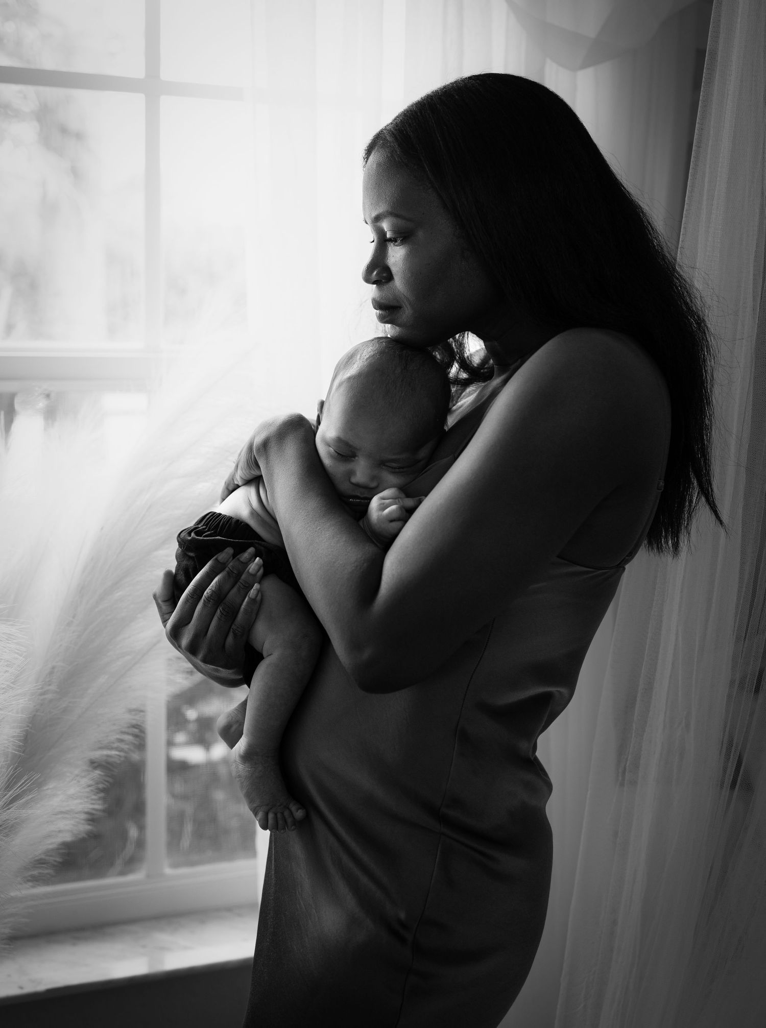 Black and white photo series showing tender moments between parent and newborn by window in silhouette.