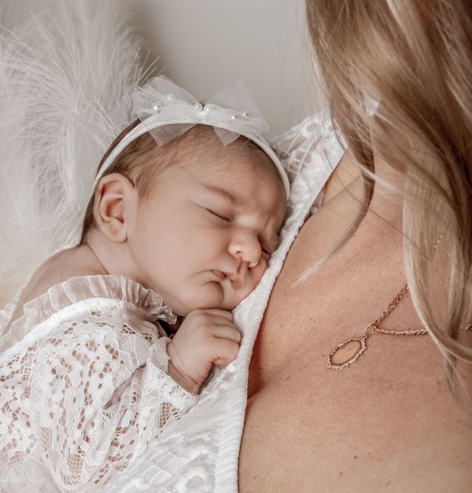 A sleeping baby rests peacefully against a shoulder in a delicate white lace outfit.
