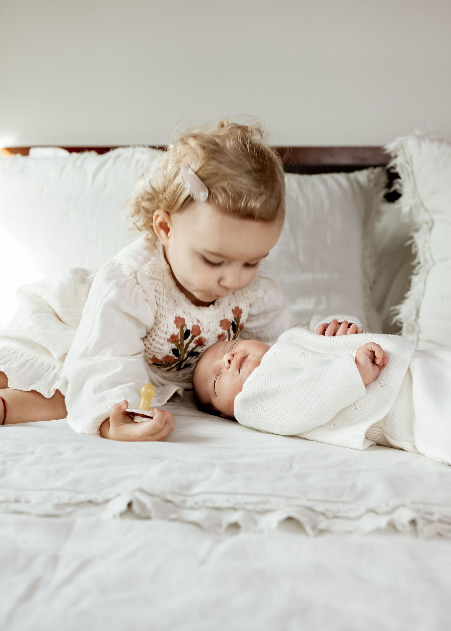 Two children in white clothing share a tender moment together on white bedding.