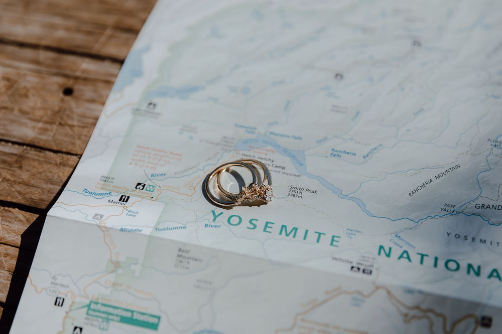 Gold wedding and engagement rings resting on a Yosemite National Park map on a rustic wooden surface.