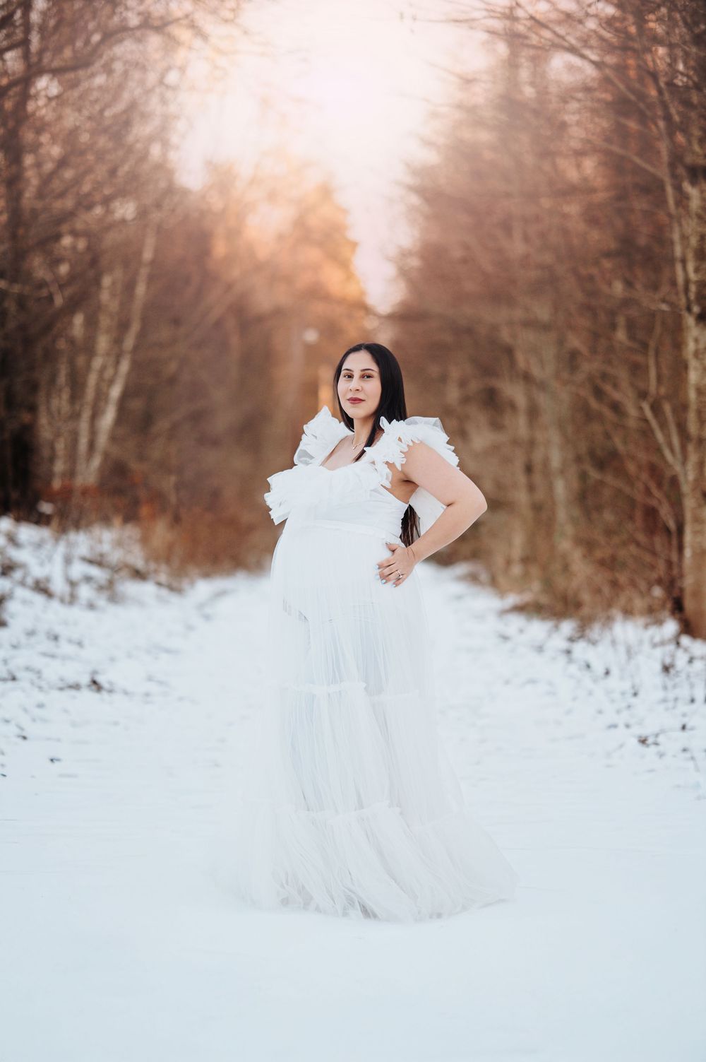 Ethereal maternity photos in white flowing dress against snowy winter landscape.