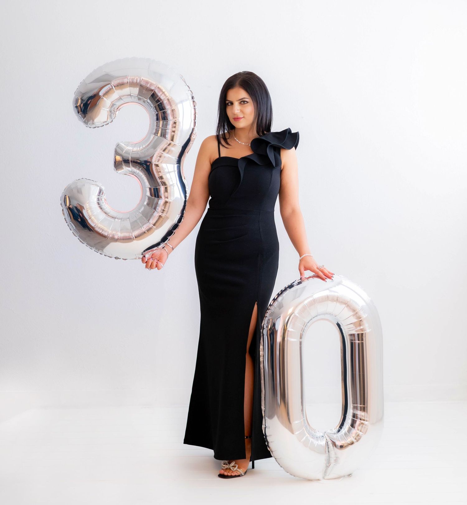 Stylish photoshoot with silver number balloons and black dress against white background.