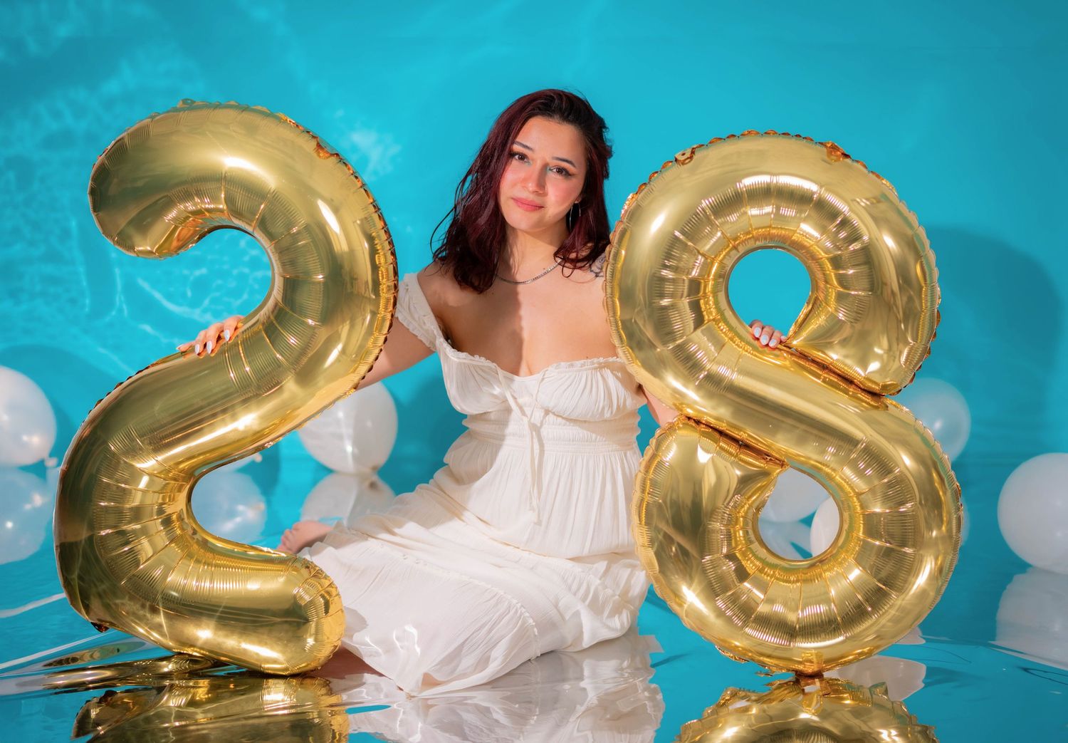 Celebration photoshoot with gold number balloons against turquoise backdrop.
