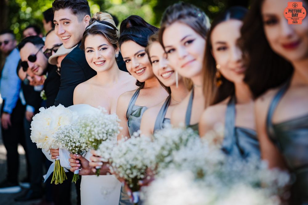 Bridesmaids in silver dresses holding white bouquets lined up outdoors at a wedding ceremony.
