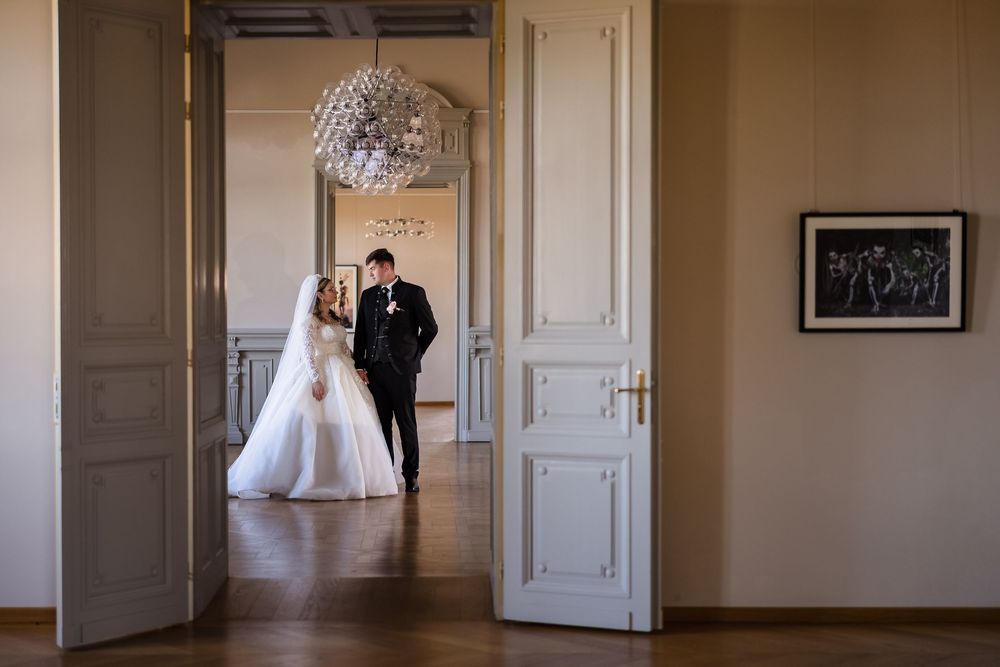 Bride and groom share a romantic moment in an elegant white room with chandelier during their wedding day.