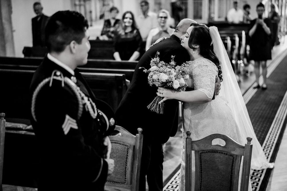 Black and white wedding photo of bride and groom sharing a kiss at the altar inside a church.