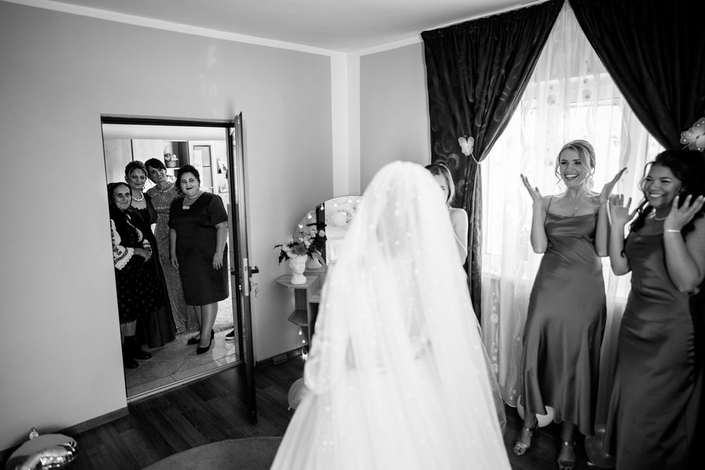 Black and white photo of a bride in a white gown and veil surrounded by bridesmaids in a dressing room.