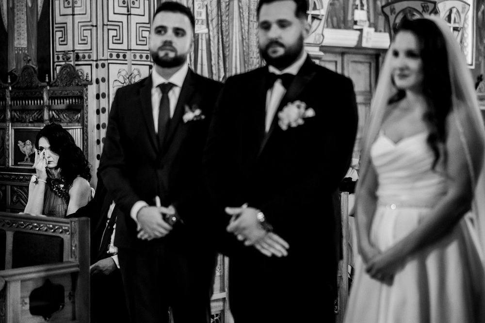Black and white wedding photo of groom and best man standing at altar with bride in white dress.