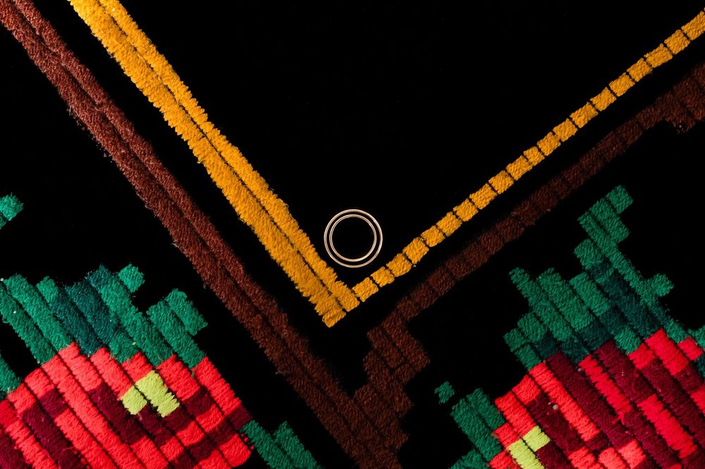 Colorful woven textile with geometric patterns in red, green, yellow, and brown on black background.
