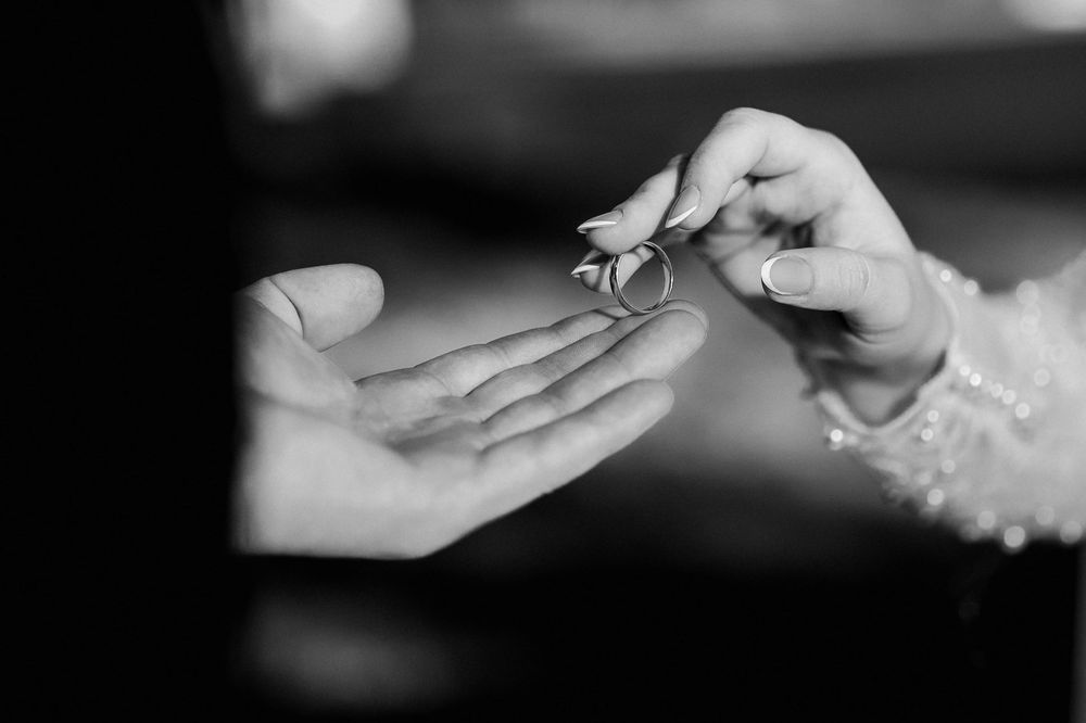 Black and white photo of hands exchanging wedding rings during a marriage ceremony.