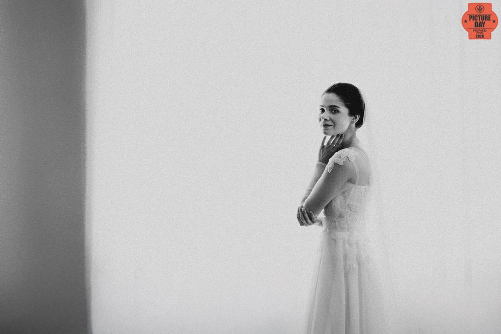 Black and white photo of a smiling bride in a white gown and veil, elegantly posed against a light wall.