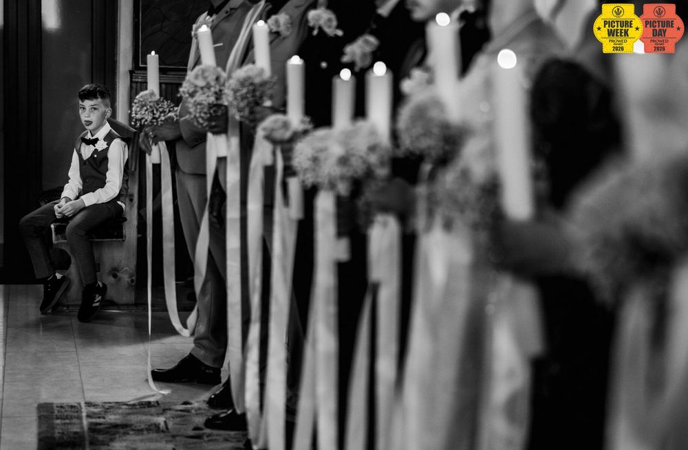 Black and white wedding ceremony photo with candles, floral arrangements, and a young boy sitting alone in the background.