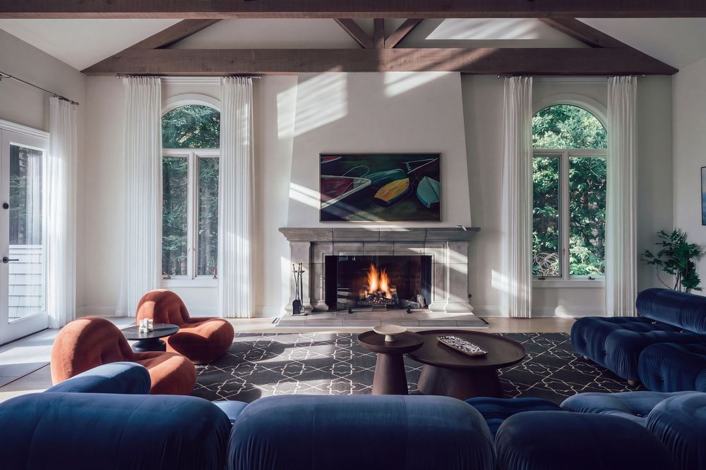 Elegant living room with blue velvet sofas, terracotta chairs, lit fireplace, arched windows, and wood beam ceiling.