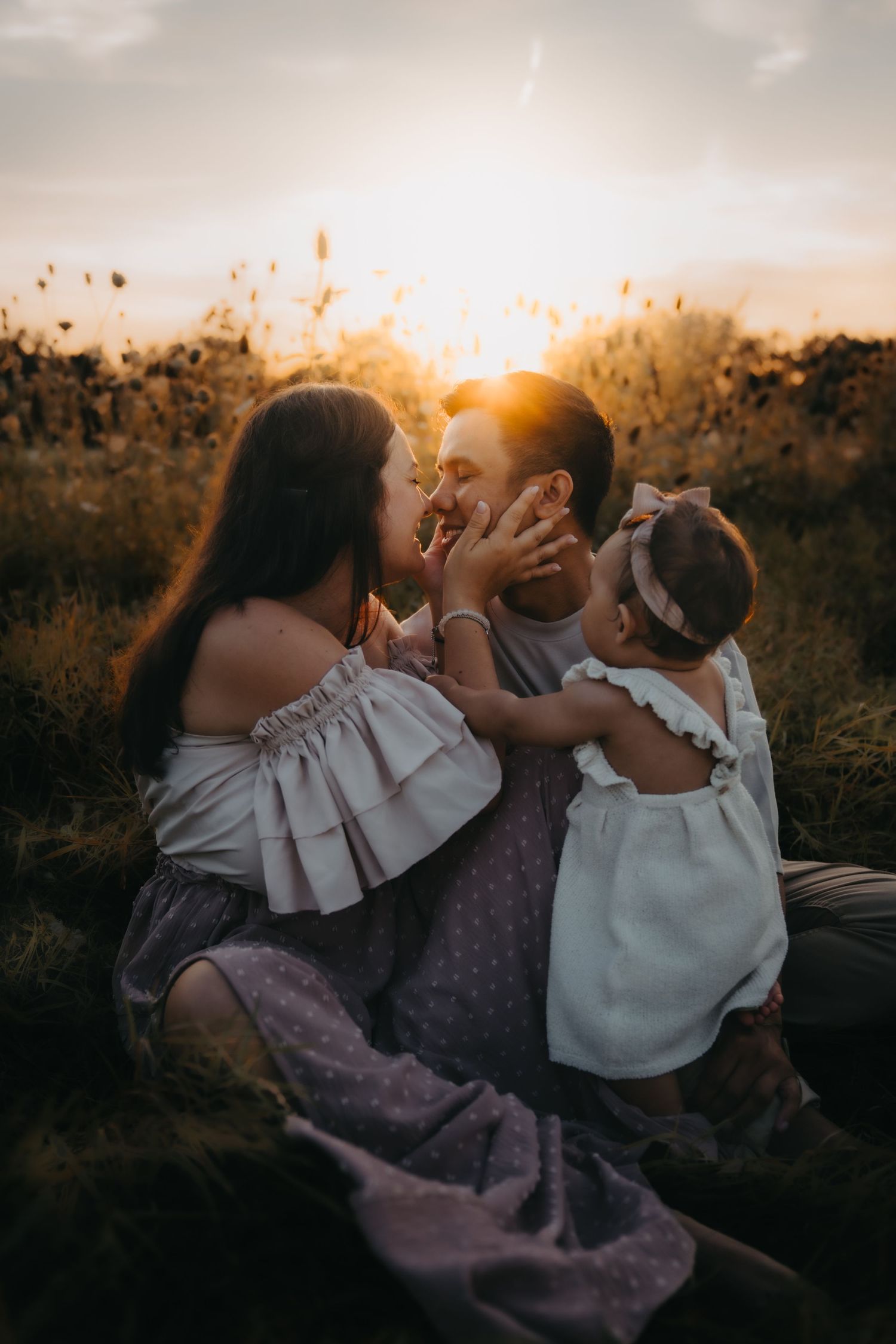 Family sharing intimate moment together in field during golden sunset.