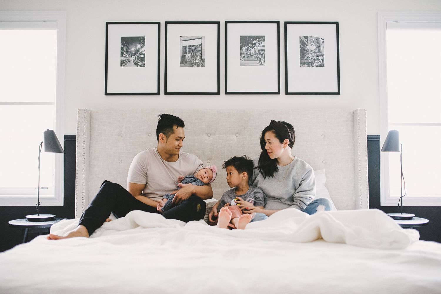 A relaxed family moment on a white bed with framed photos decorating the wall above.