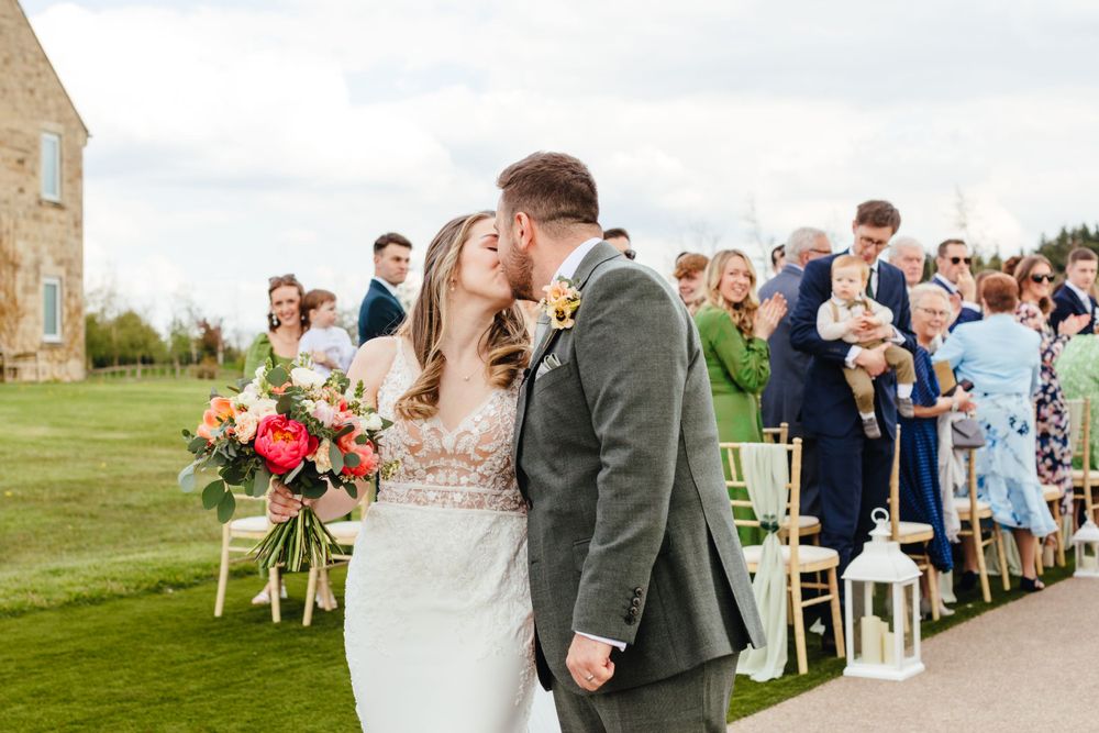 Wedding celebration on manicured lawn with guests watching couple's first kiss.