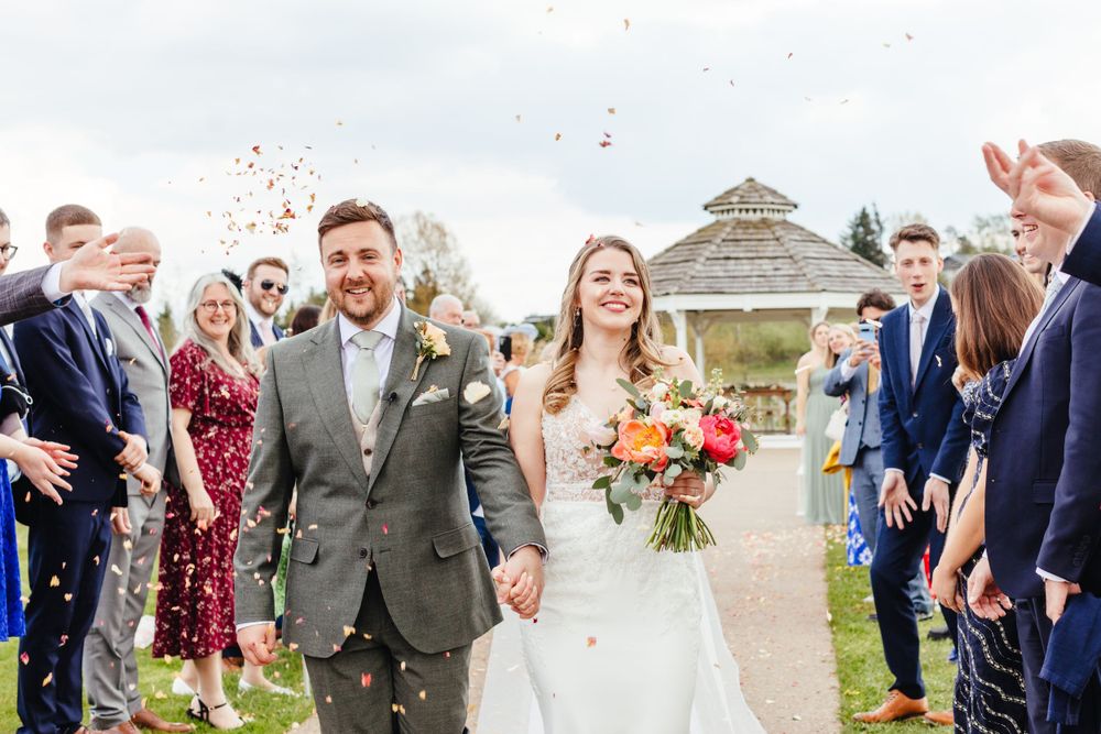 Joyful wedding exit with guests throwing confetti as couple walks down aisle outdoors.