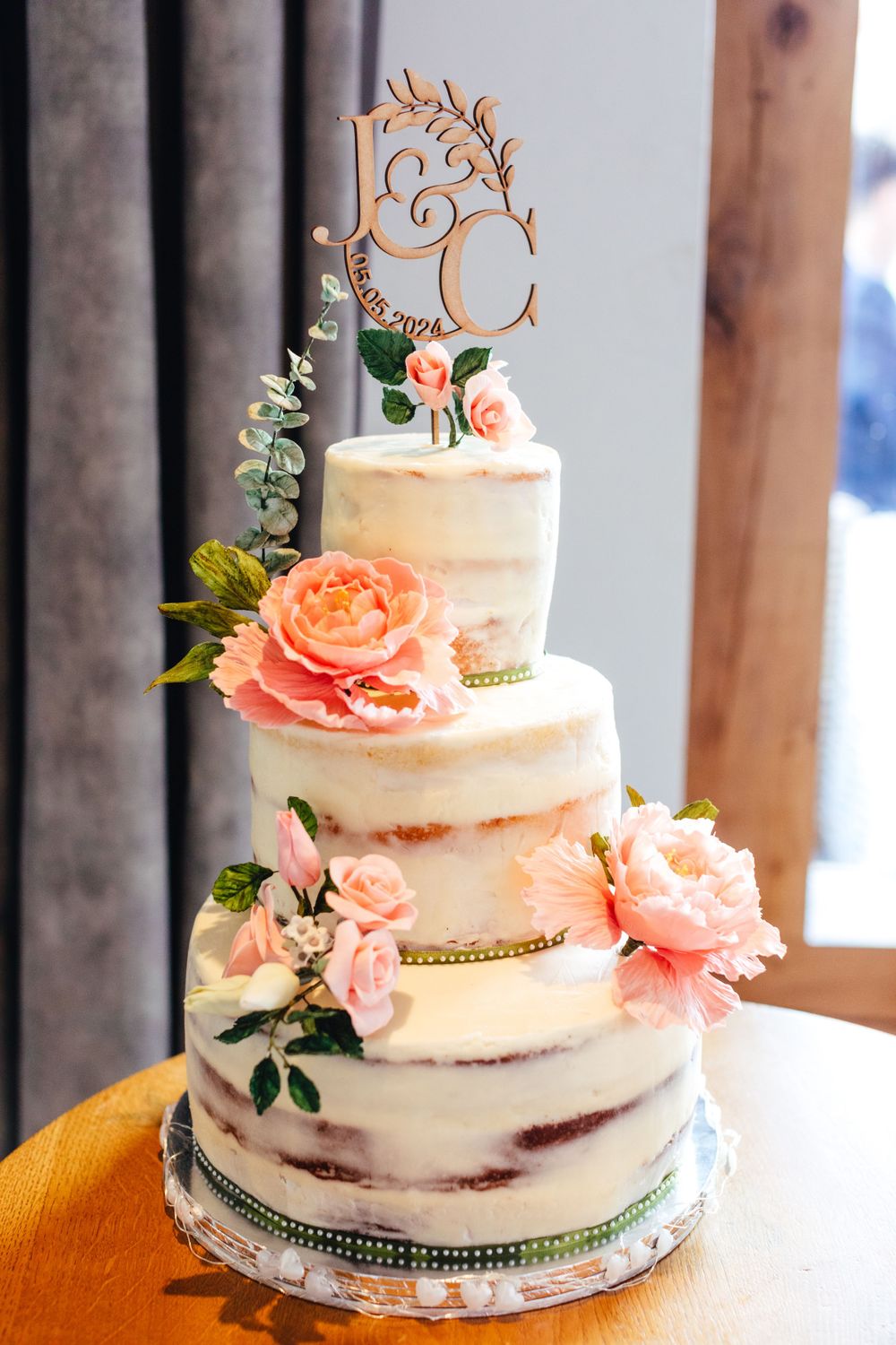 Four-tier semi-naked wedding cake decorated with peach roses and custom wooden topper.