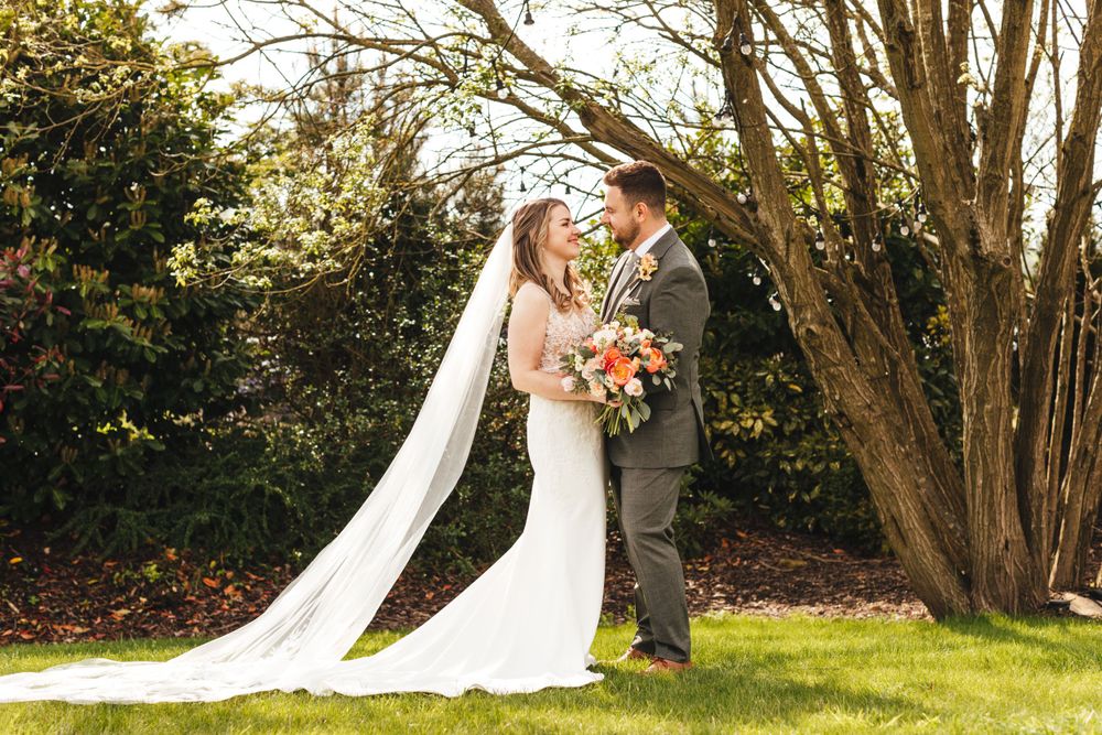 Garden wedding portrait with flowing veil and colorful bouquet against natural backdrop.
