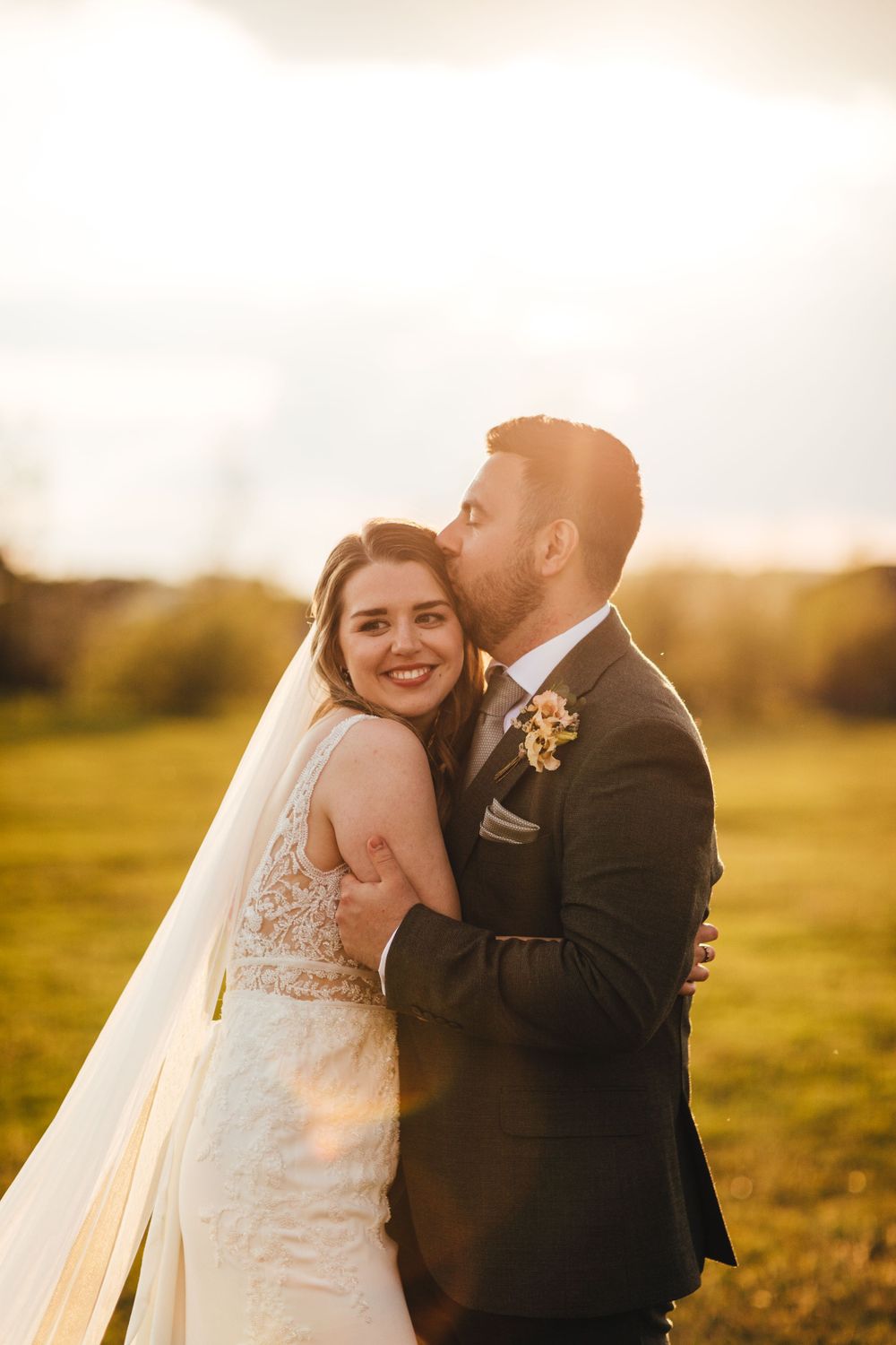 Intimate wedding portrait of newlyweds embracing in warm sunset light.