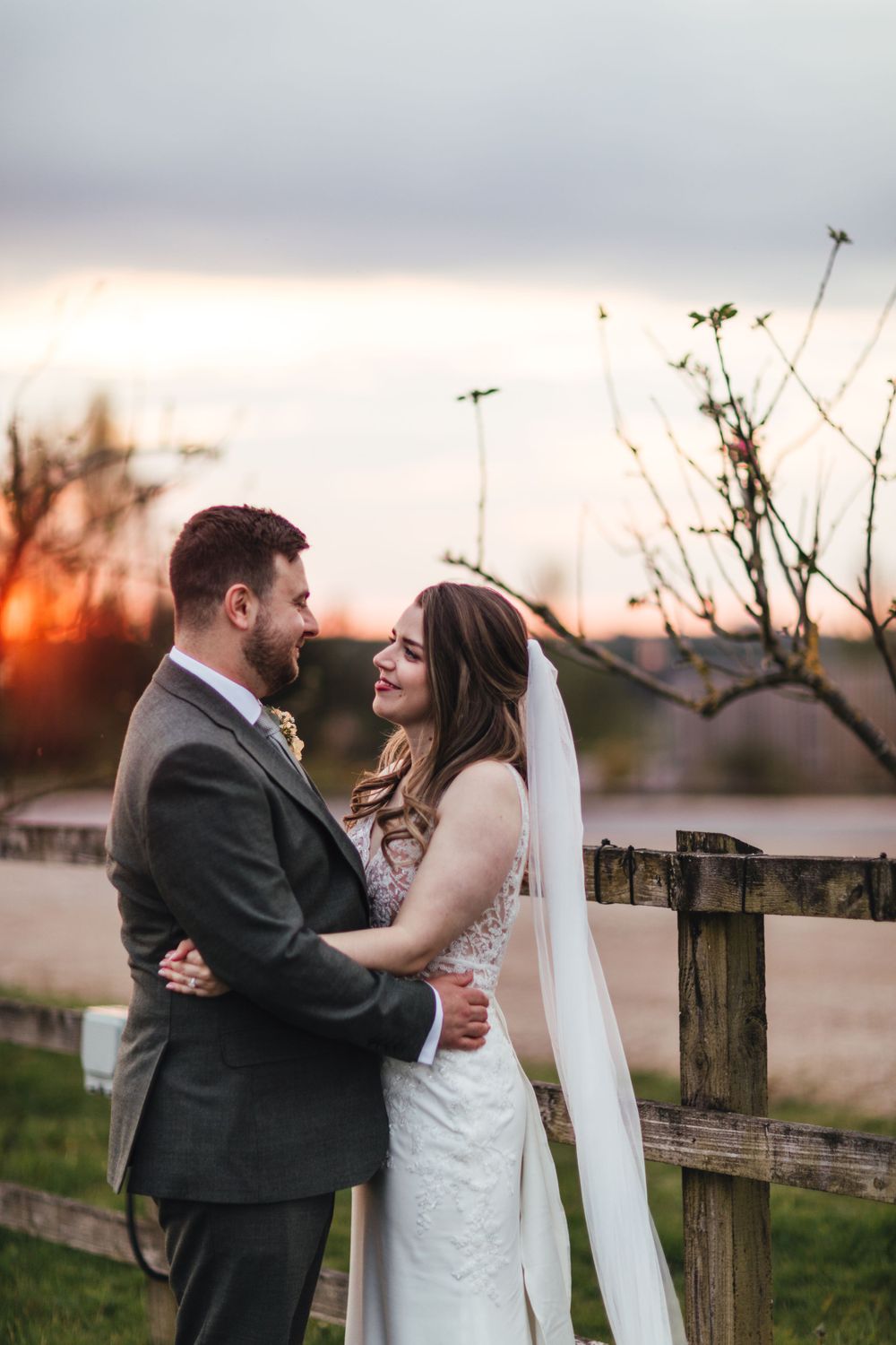 Romantic sunset wedding photo by a rustic wooden fence.
