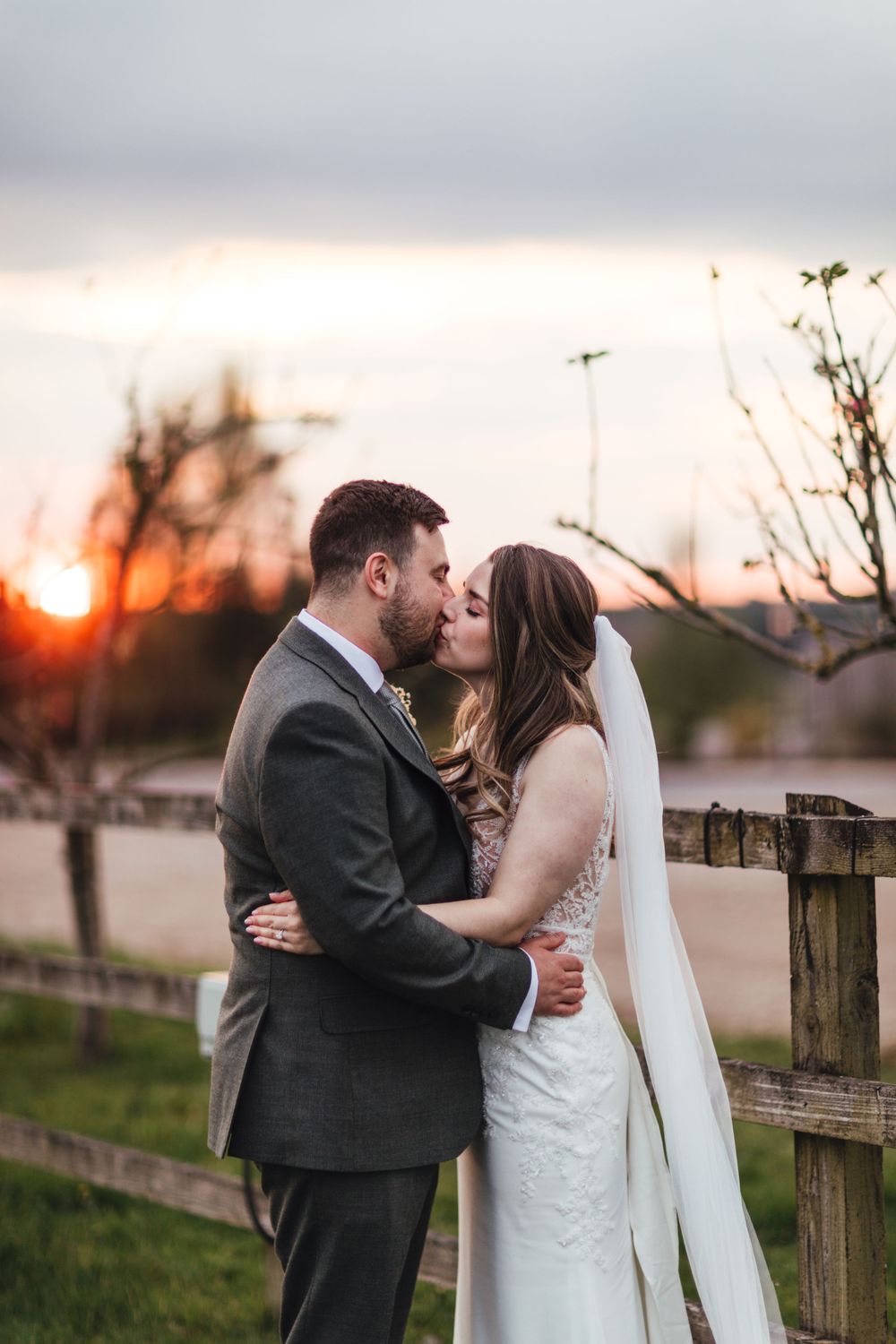 Wedding couple sharing an intimate moment by wooden fence at sunset.
