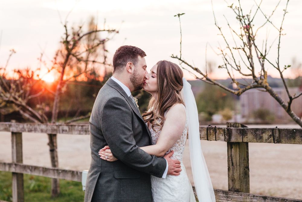 Romantic sunset wedding portrait with couple embracing near rustic fence.