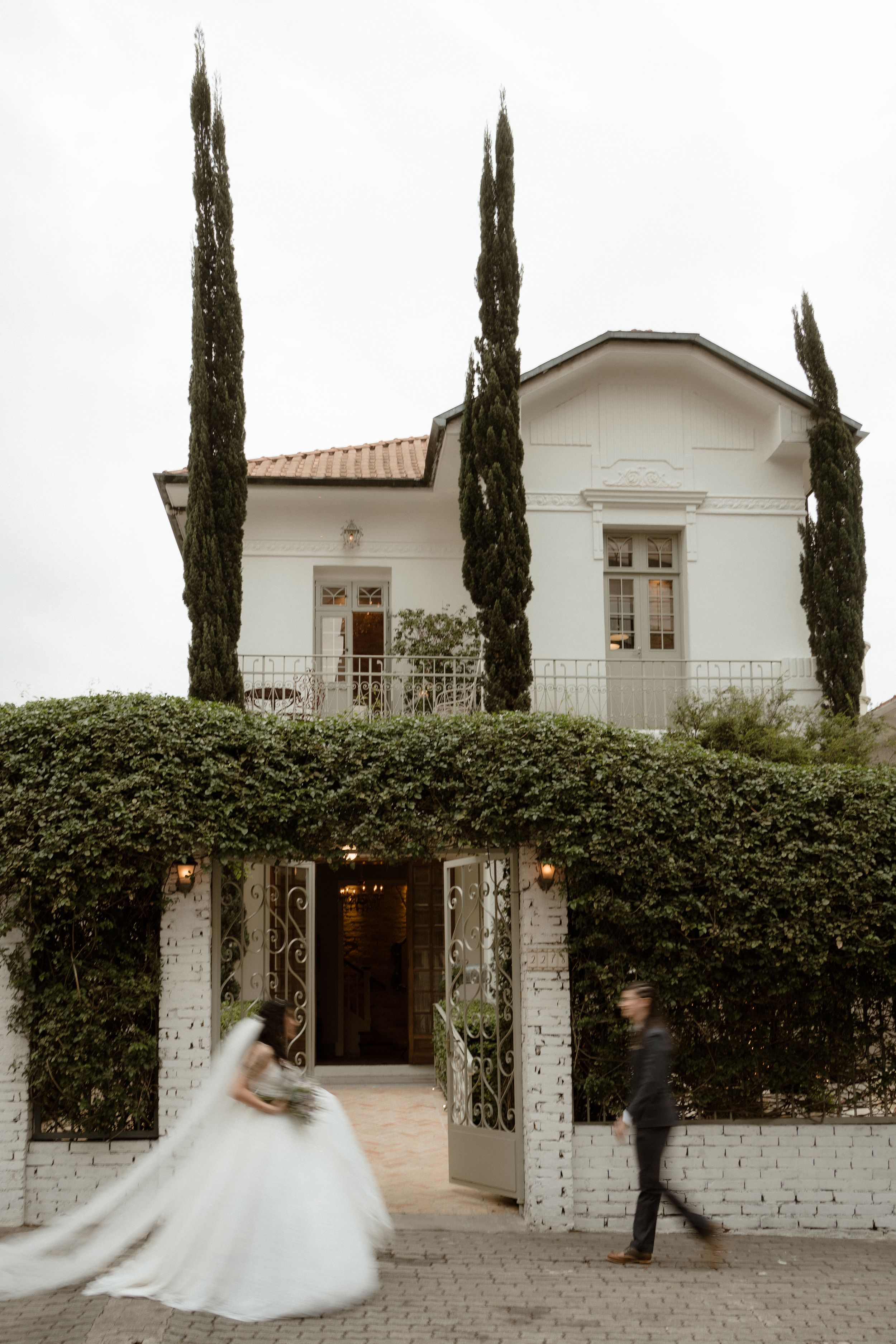 Mediterranean-style white mansion with cypress trees and climbing vines creates elegant wedding venue backdrop.