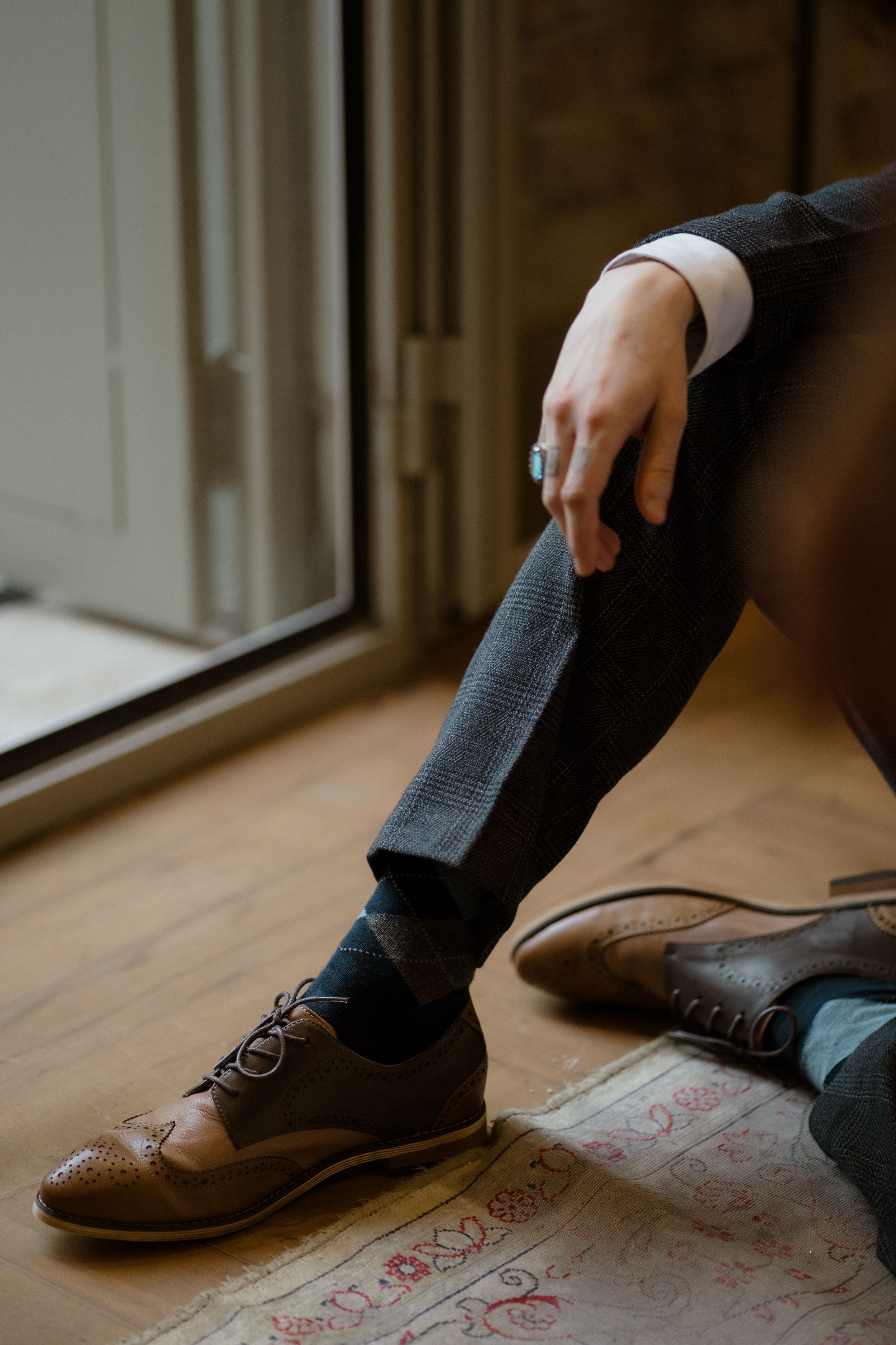 Getting ready moment showing dark socks and vintage-style shoes on patterned floor.