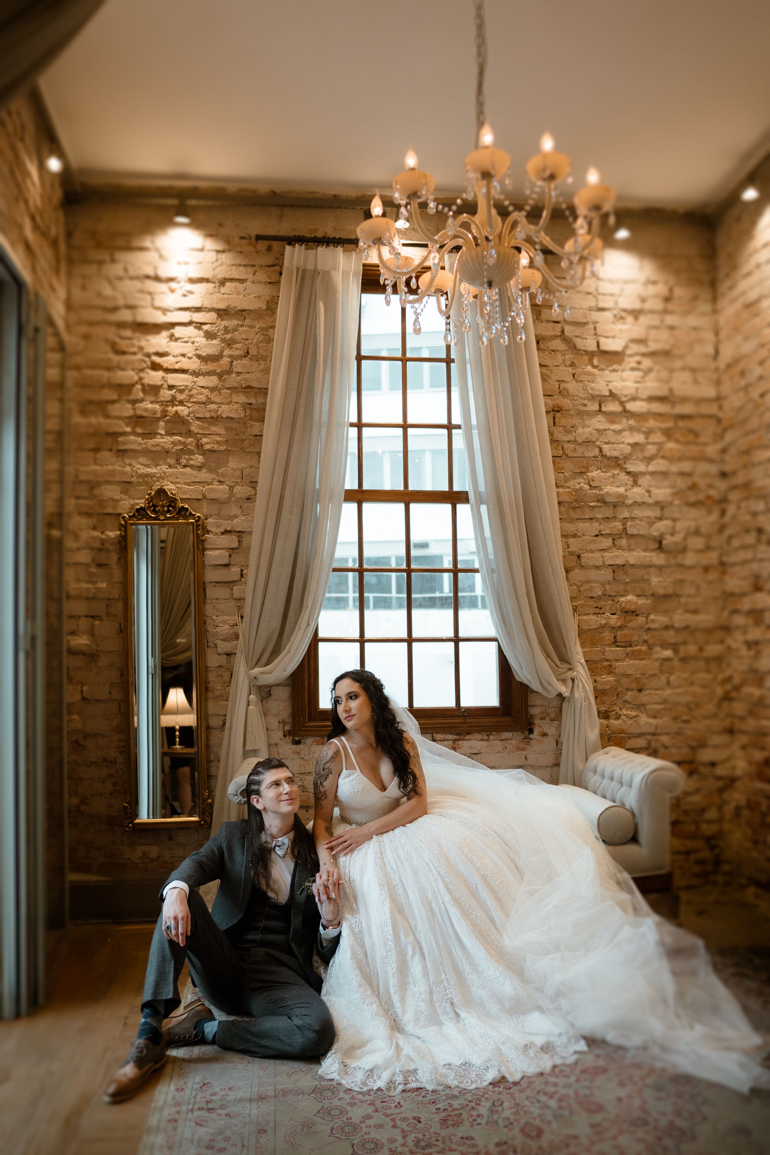 Elegant wedding portraits in rustic room with exposed brick walls and white curtains.