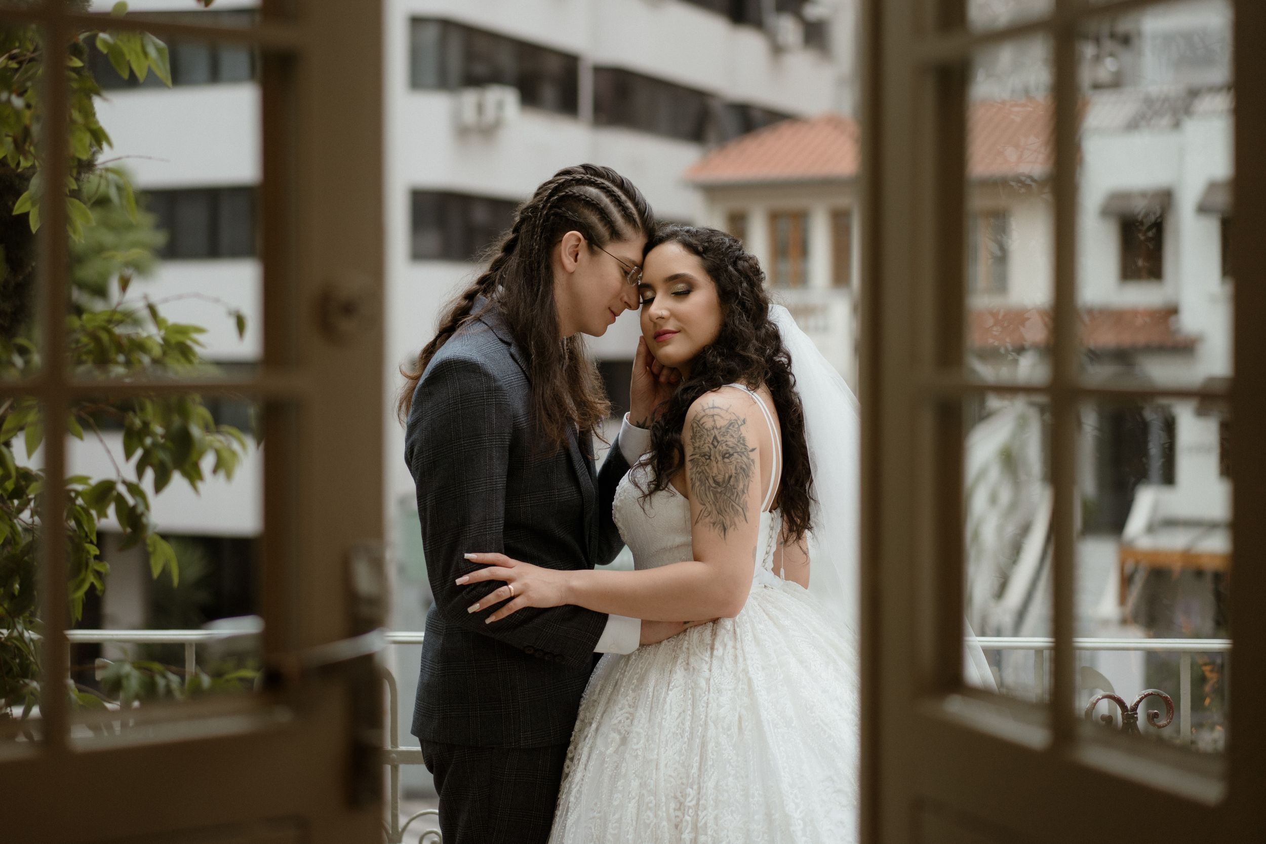 A romantic wedding couple sharing an intimate moment on a balcony in formal attire.