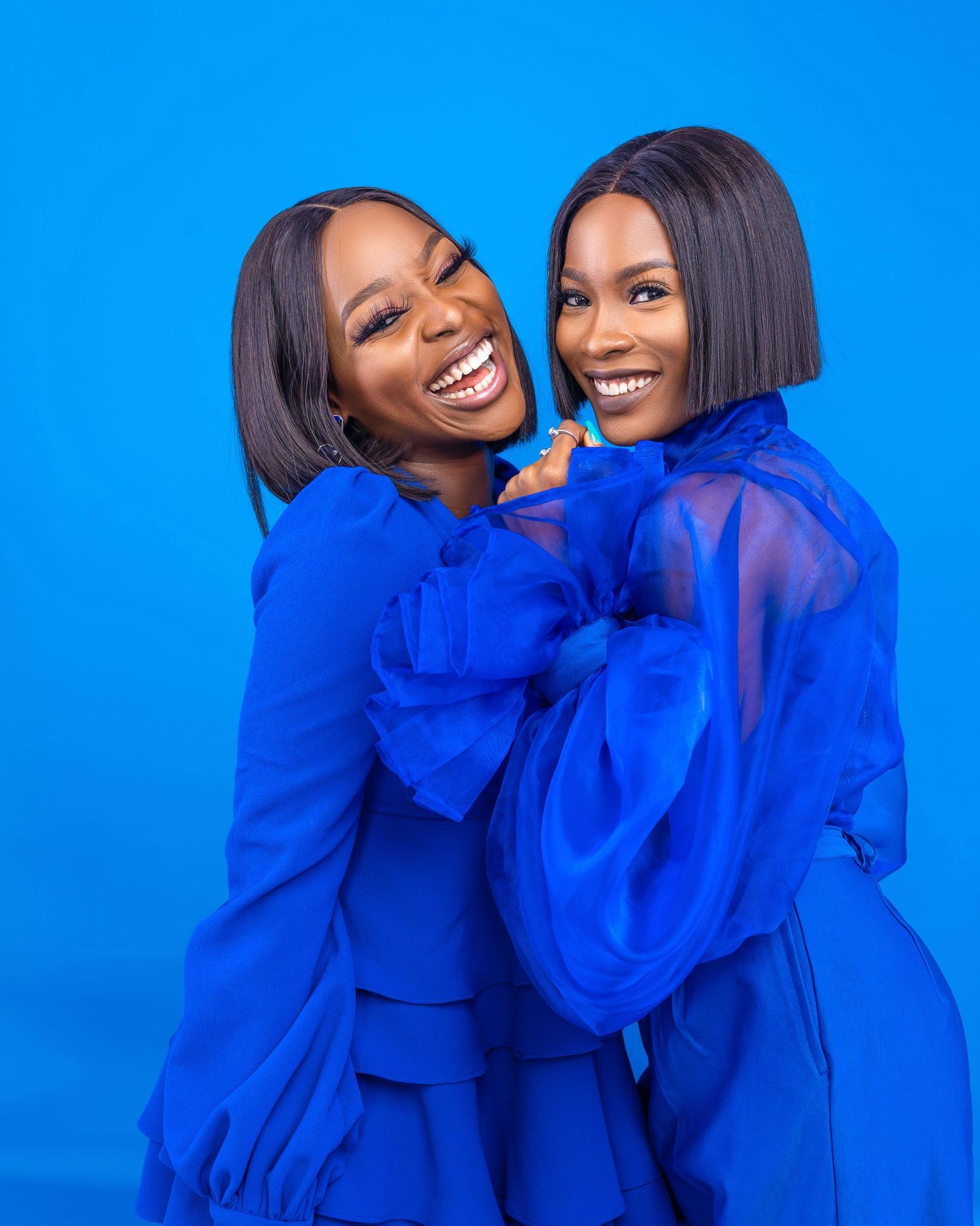 Two people in vibrant royal blue outfits posing against a bright blue background.