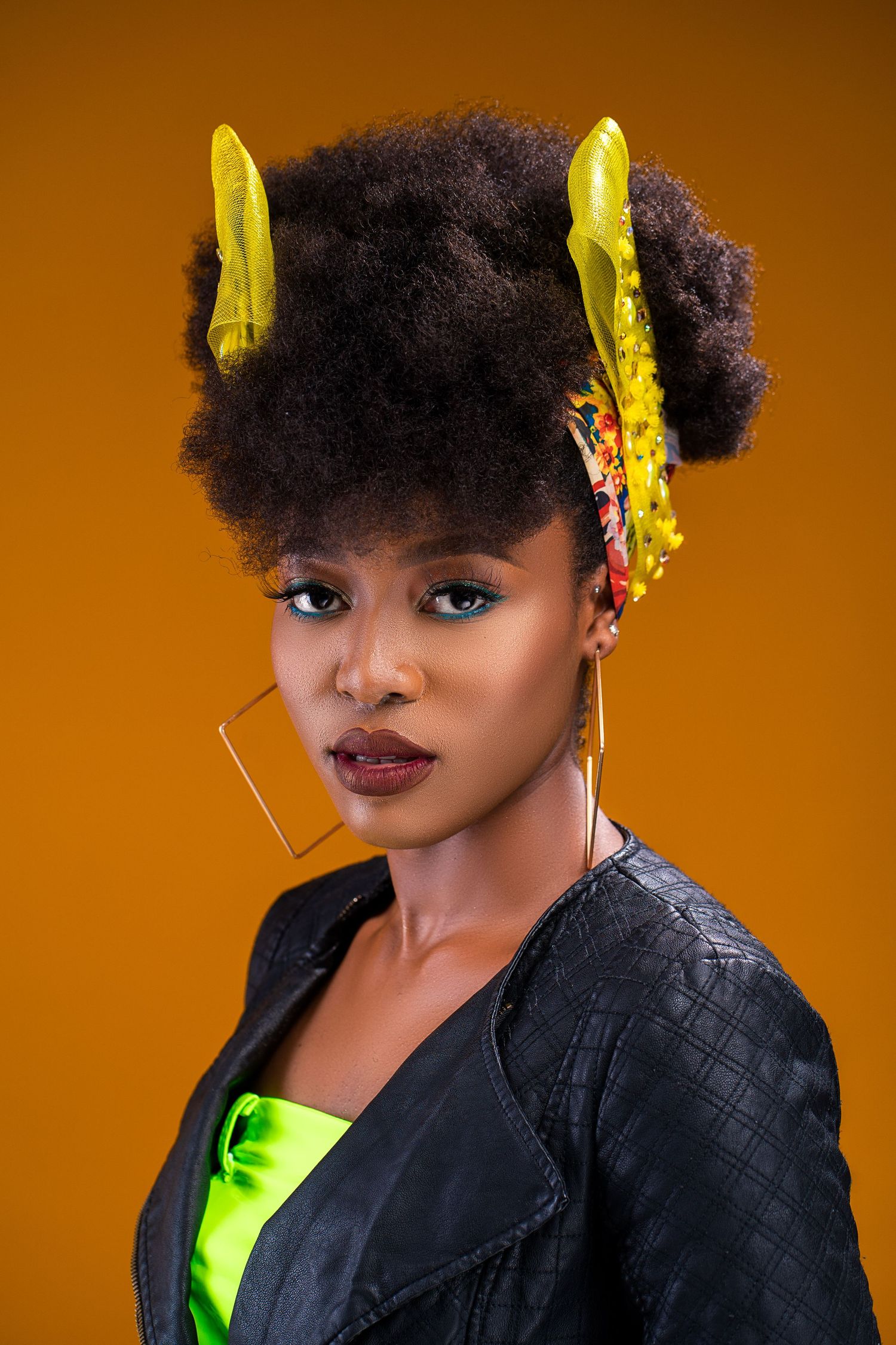 Creative portrait with natural hair styled with yellow accessories against an orange background.