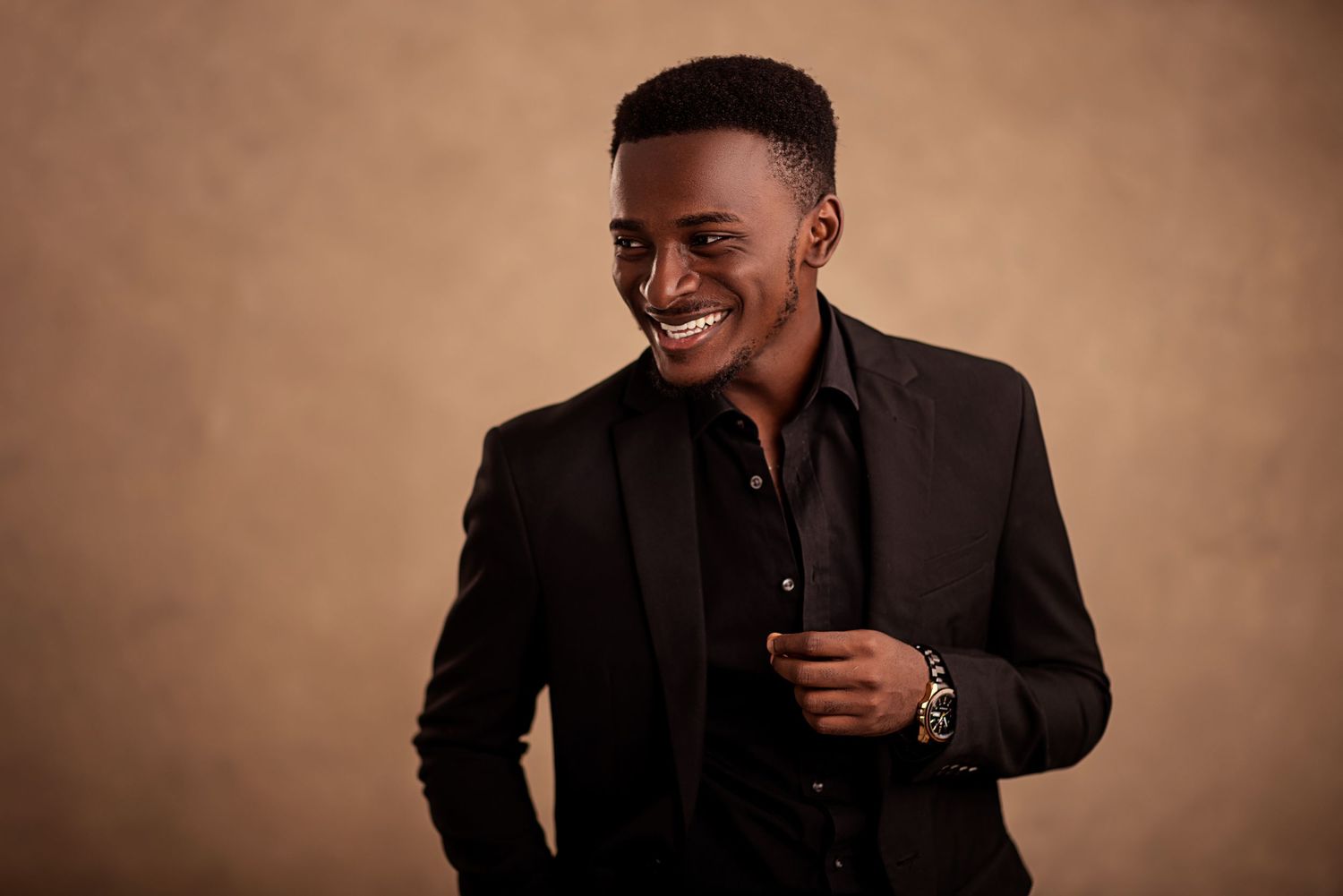 Professional portrait of person in dark suit smiling against warm brown backdrop.