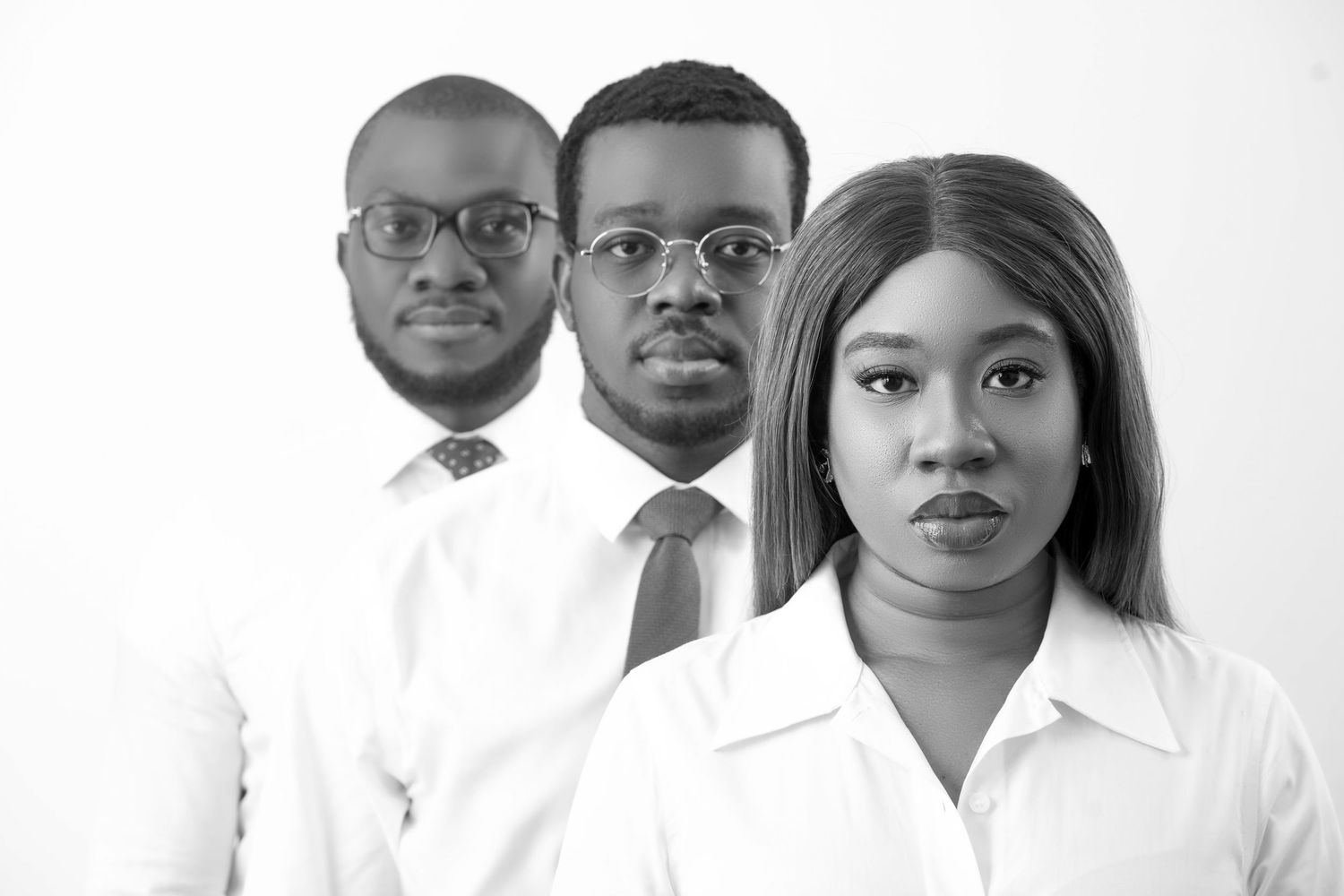 Professional corporate team photo of three business people in white shirts against white background.