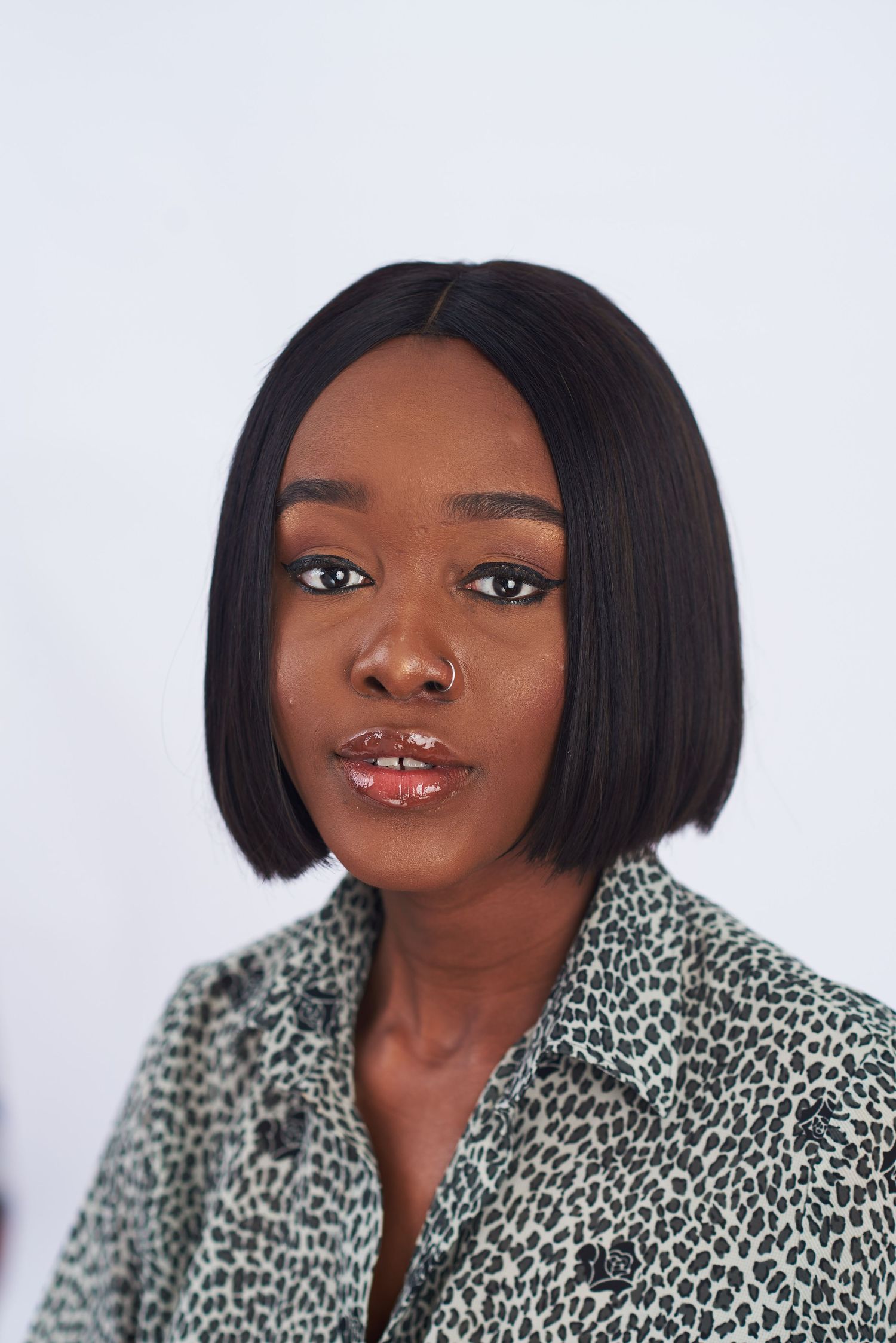 Professional headshot with short black hair wearing animal print top against white background.