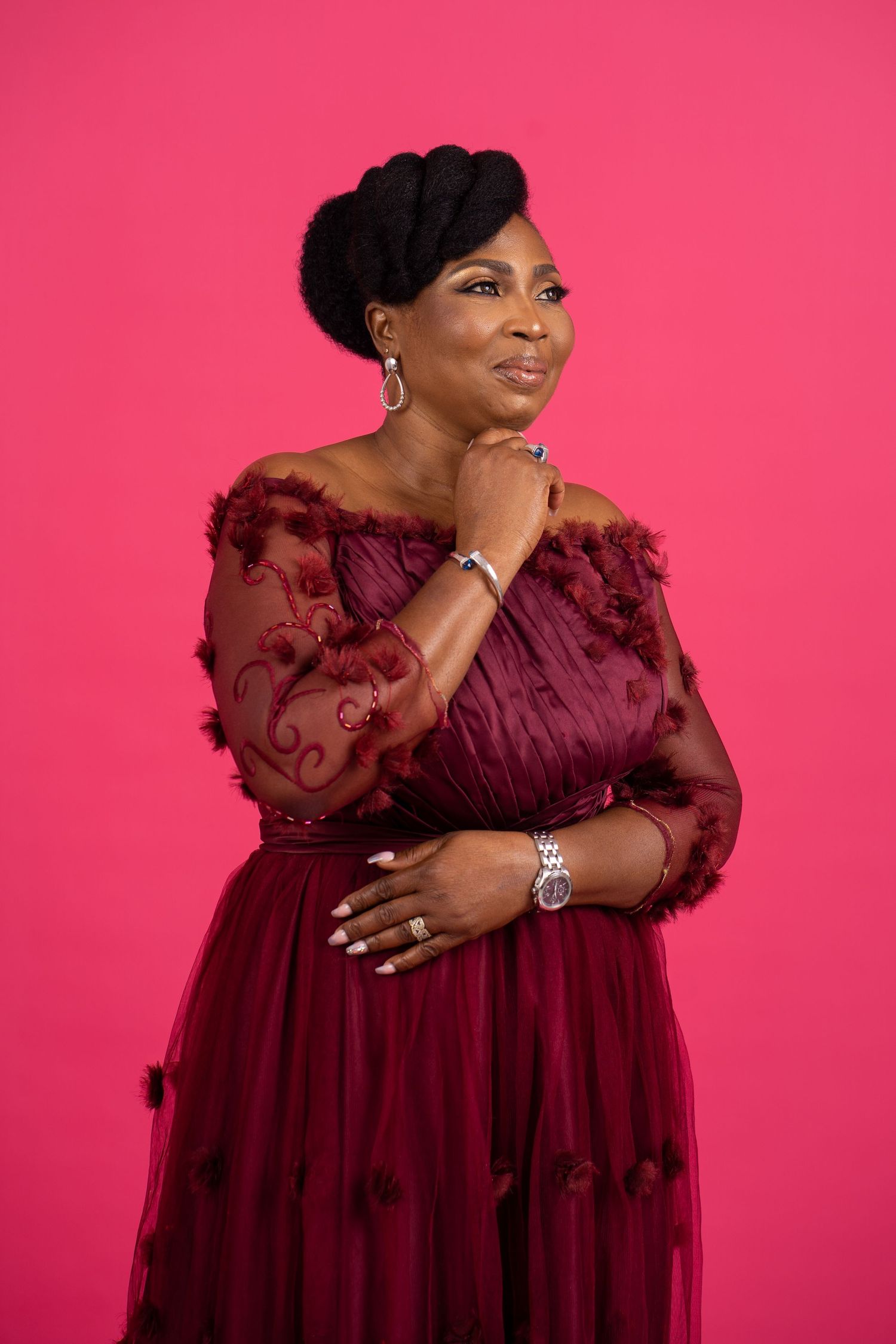 Elegant portrait in a burgundy off-shoulder gown with lace details against a pink backdrop.