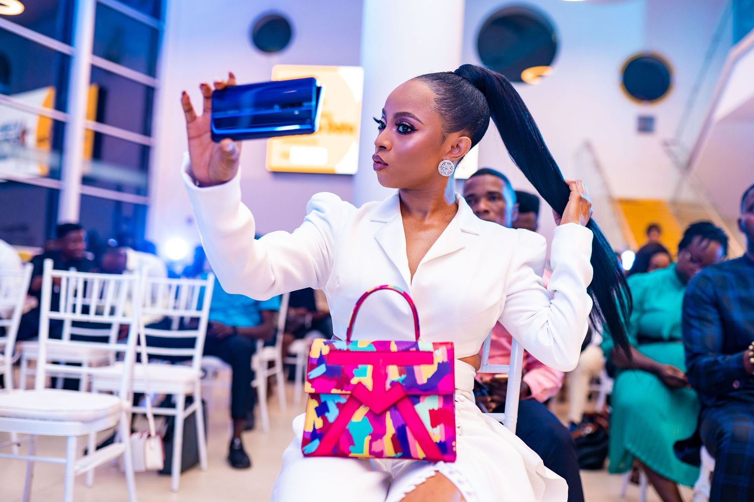 Fashionable person taking a selfie while holding a pink shopping bag at an event venue.
