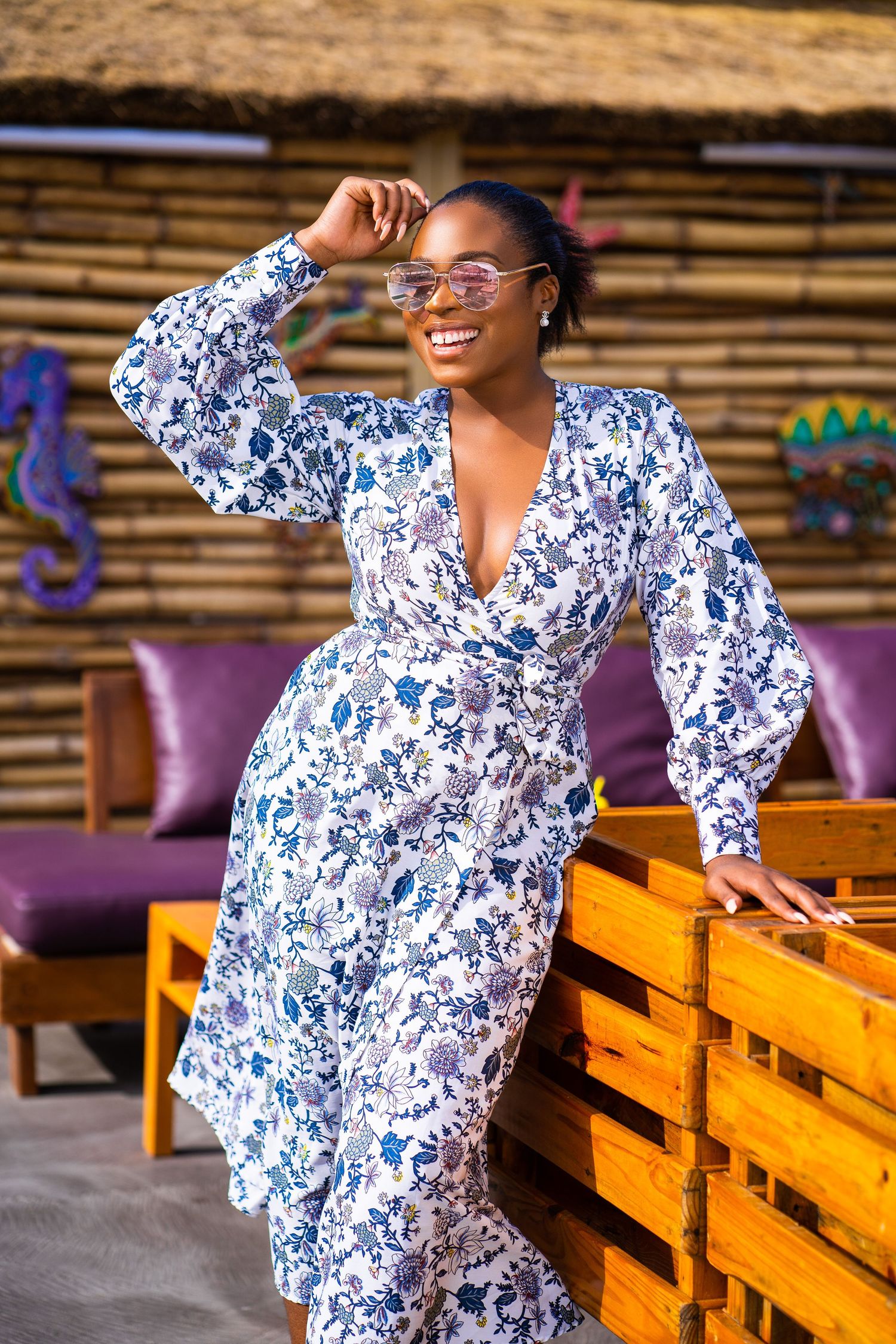 Portrait in blue and white floral wrap dress posing near wooden crates.