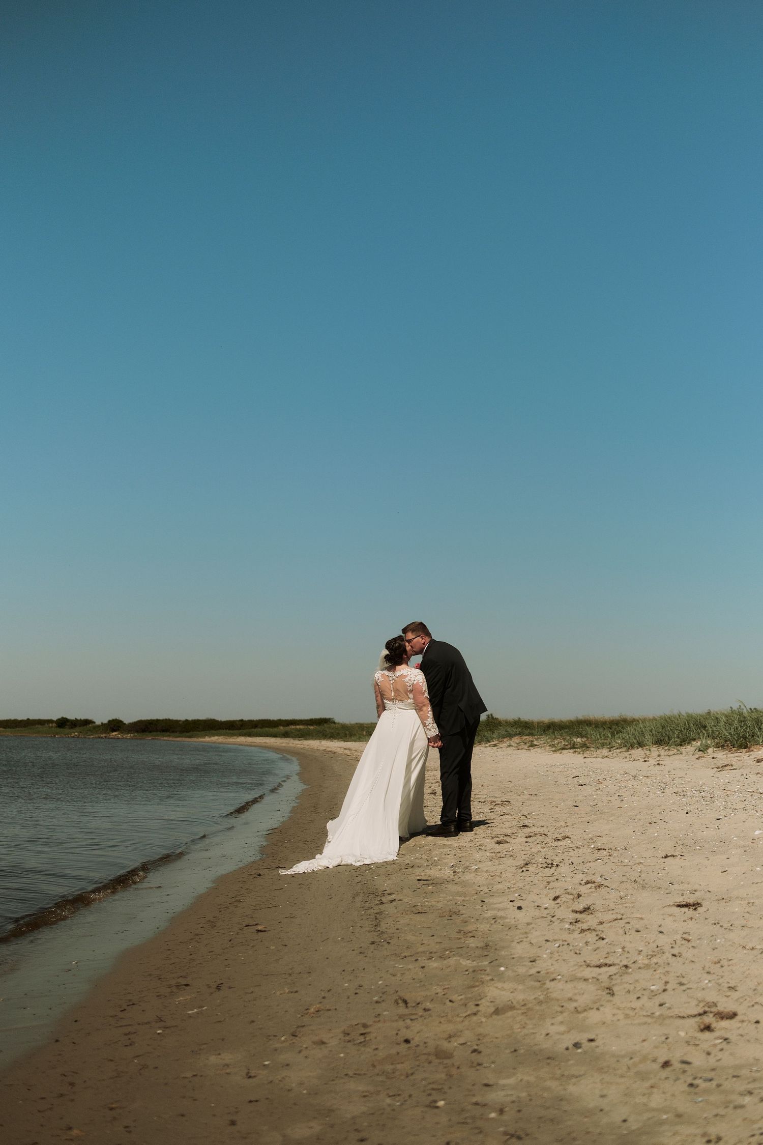 A couple in wedding attire sharing an intimate moment on a beach shoreline.