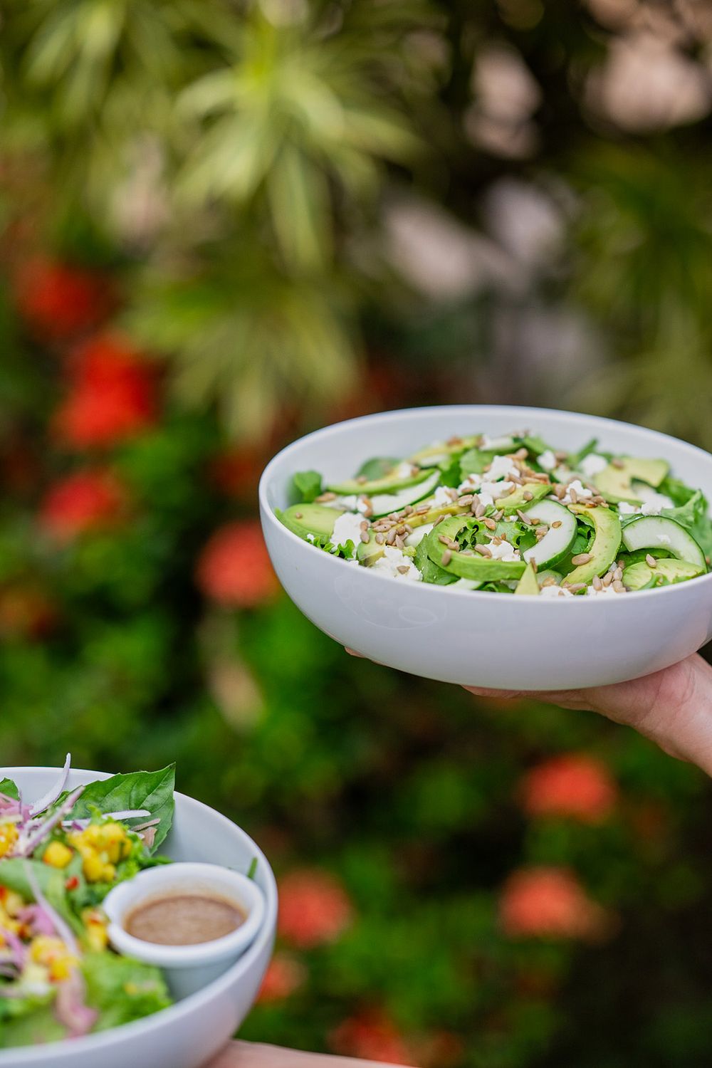 A fresh summer salad of cucumber, herbs and edamame in a white bowl is served outdoors with a side of dressing.